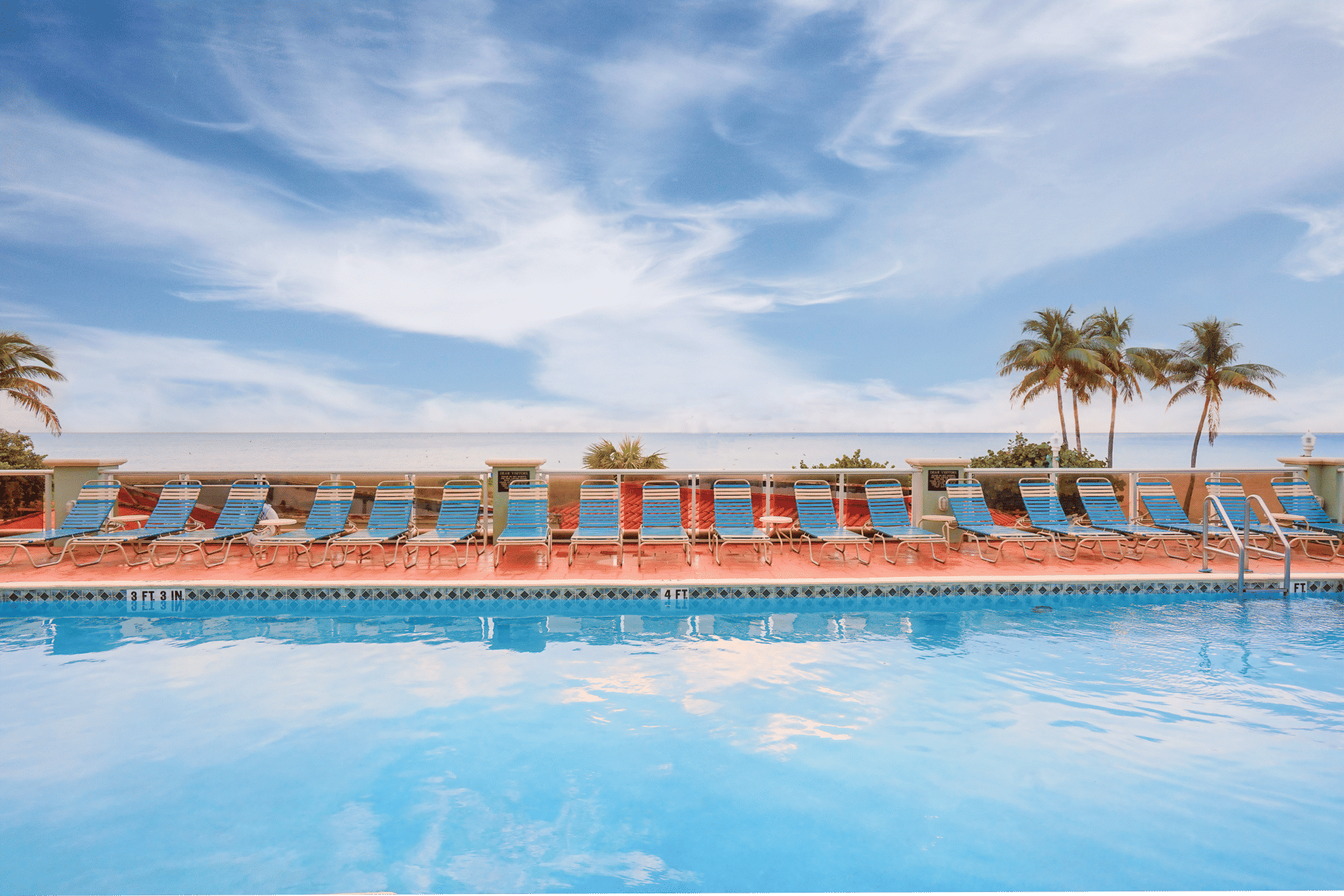 image Pool Area: Swimming pool area with lounge chairs and palm trees, set against a blue sky.