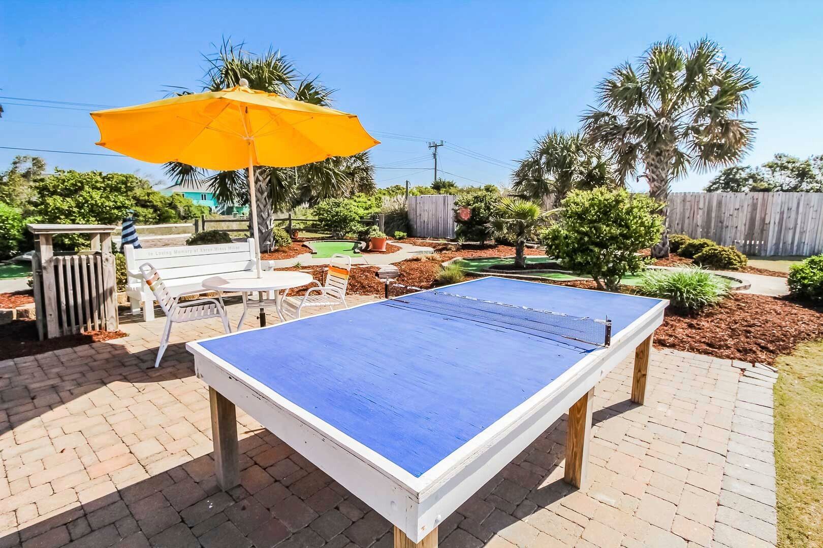 image This vibrant backyard features a blue ping pong table shaded by a bright umbrella, offering a perfect spot for family fun amidst the lush landscaping and nearby mini-golf.