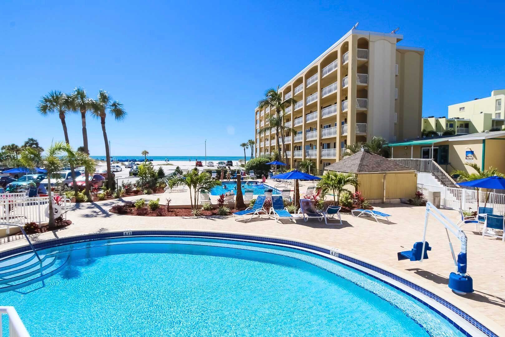 image Enjoy stunning beach views from the poolside balcony of this 2BR condo featuring a shared outdoor pool and direct beach access, surrounded by lush landscaping and palm trees.