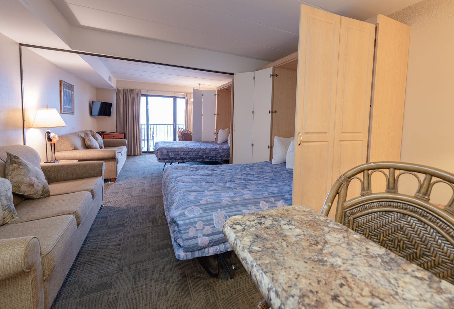 image This spacious room features two Queen Murphy beds, a cozy seating area, and a private balcony offering street views, perfect for relaxing after a day at the beach.