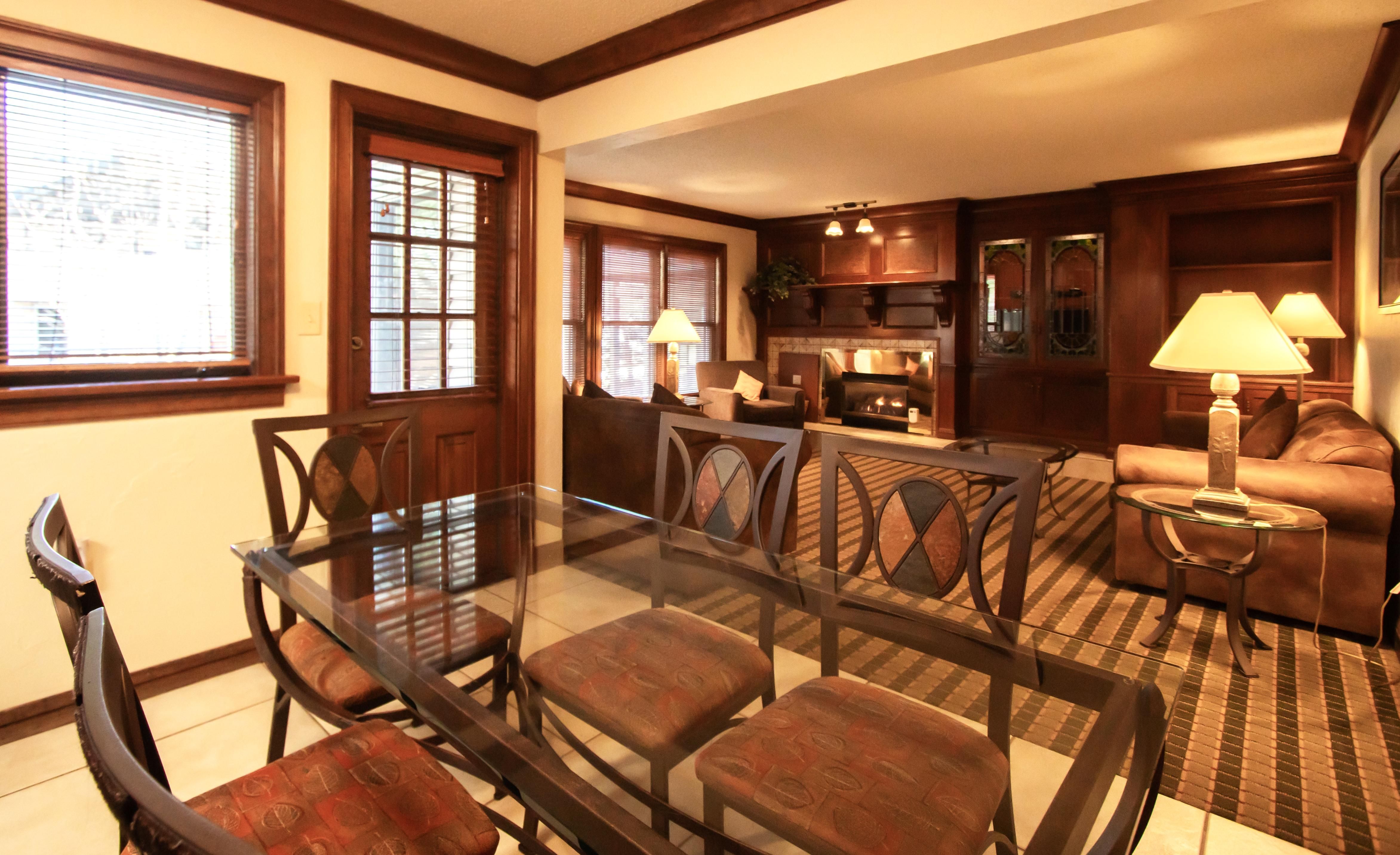 image Dining area with a glass table and comfortable seating, overlooking the inviting living space with a fireplace.