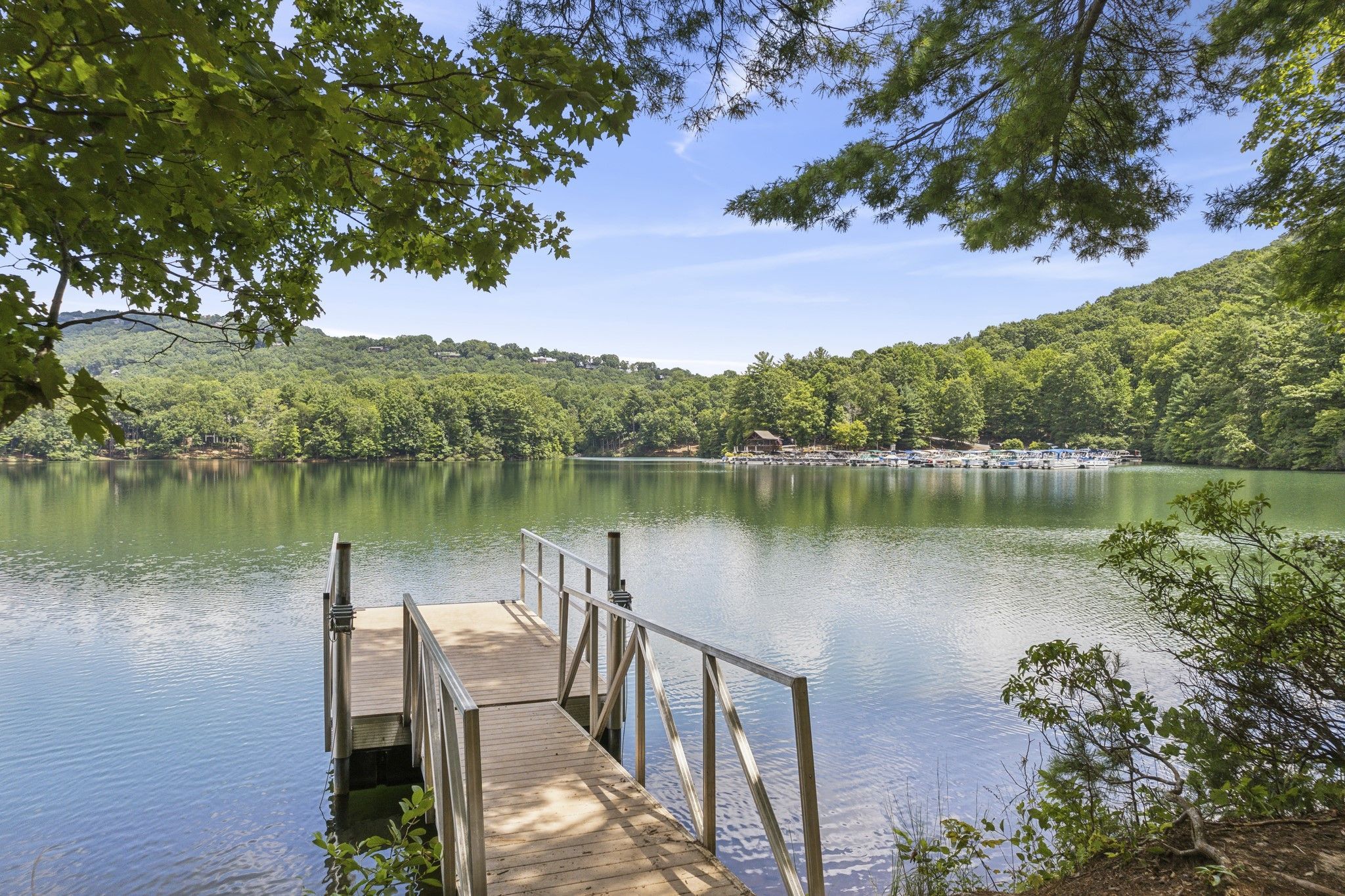 image The community lake, with a wooden dock reaching out over calm water, boats moored along the shore and forested hills beyond.
