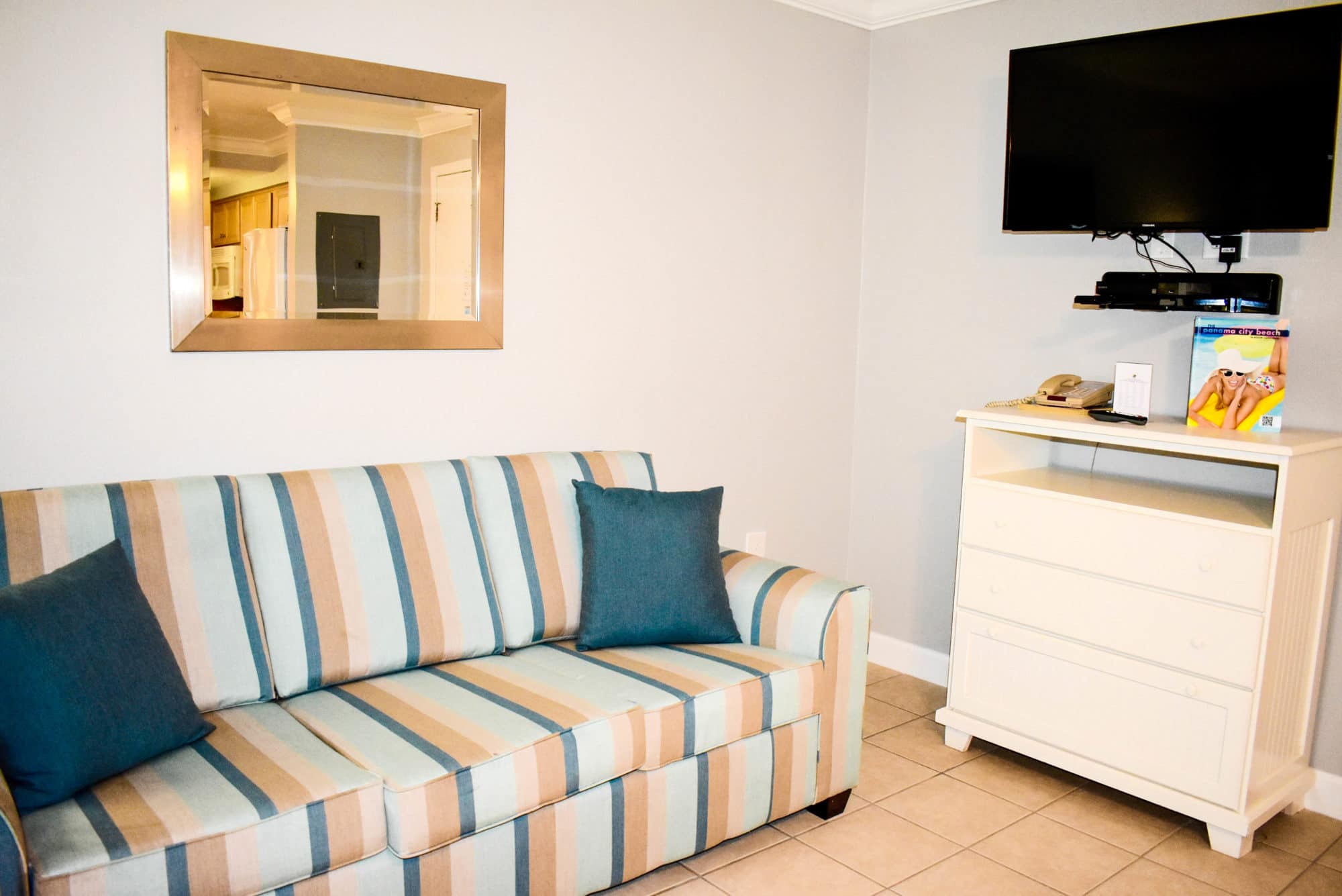 image A comfortably striped sofa adorned with teal accents warmly welcomes guests to unwind after a day at the beach, while a flat-screen TV adds a touch of modern convenience to this quaint living space.