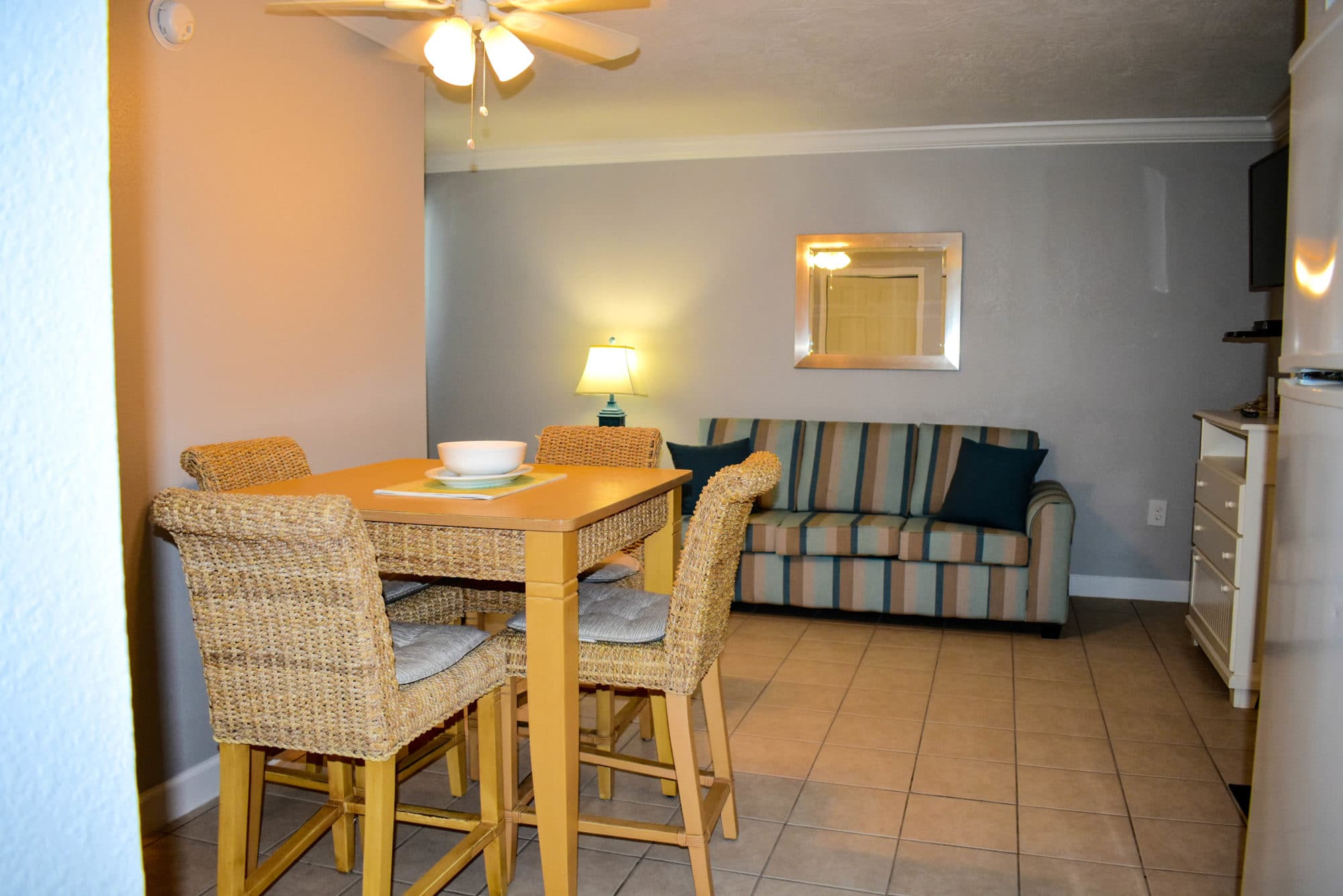 image The bright and airy living space showcases a cheerful dining area with woven chairs and a sleek table, inviting guests to enjoy meals together while surrounded by beach-inspired decor and natural light.