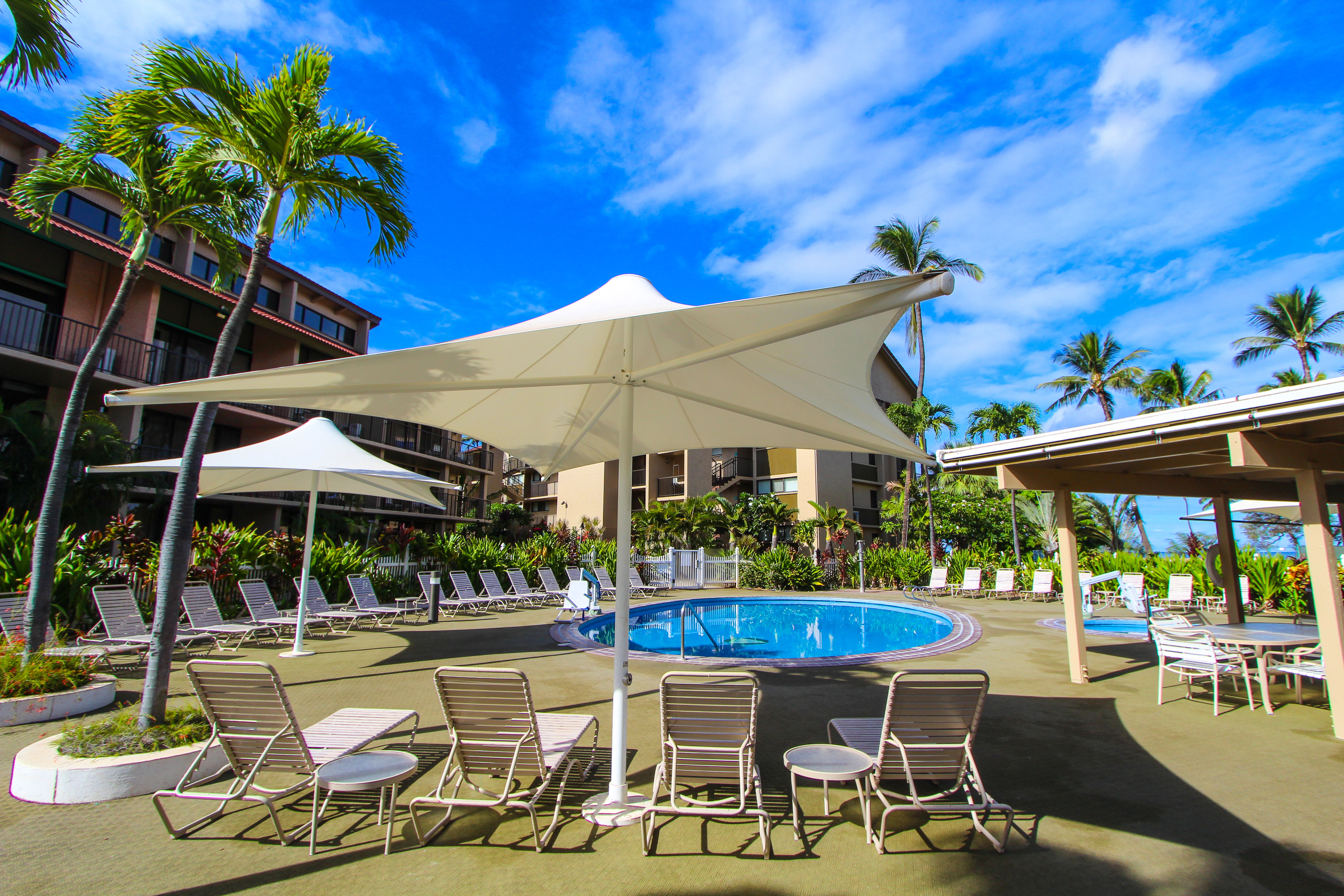 image Relax by the inviting resort pool surrounded by lush tropical landscaping and comfortable lounge chairs, perfect for sunny days in Maui.
