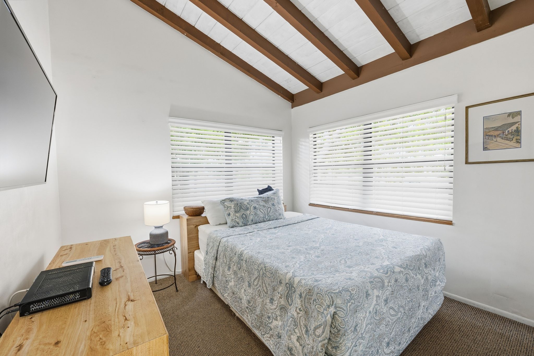 image One of the bedrooms offers a queen bed, work desk, and TV, with natural light filtering through window blinds.