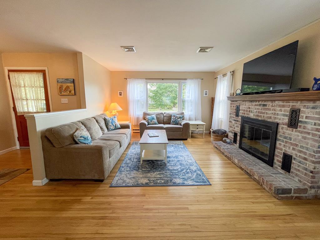 image Step into this cozy living room where sunlight dances through the windows, inviting you to relax on the plush sofas by the warmth of the wood-burning fireplace.