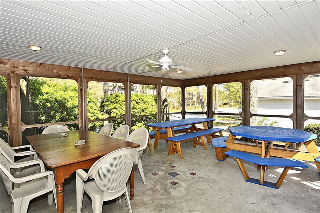 image The airy screened porch features a large wooden dining table surrounded by white chairs and multiple blue picnic-style tables, perfect for leisurely meals outdoors.