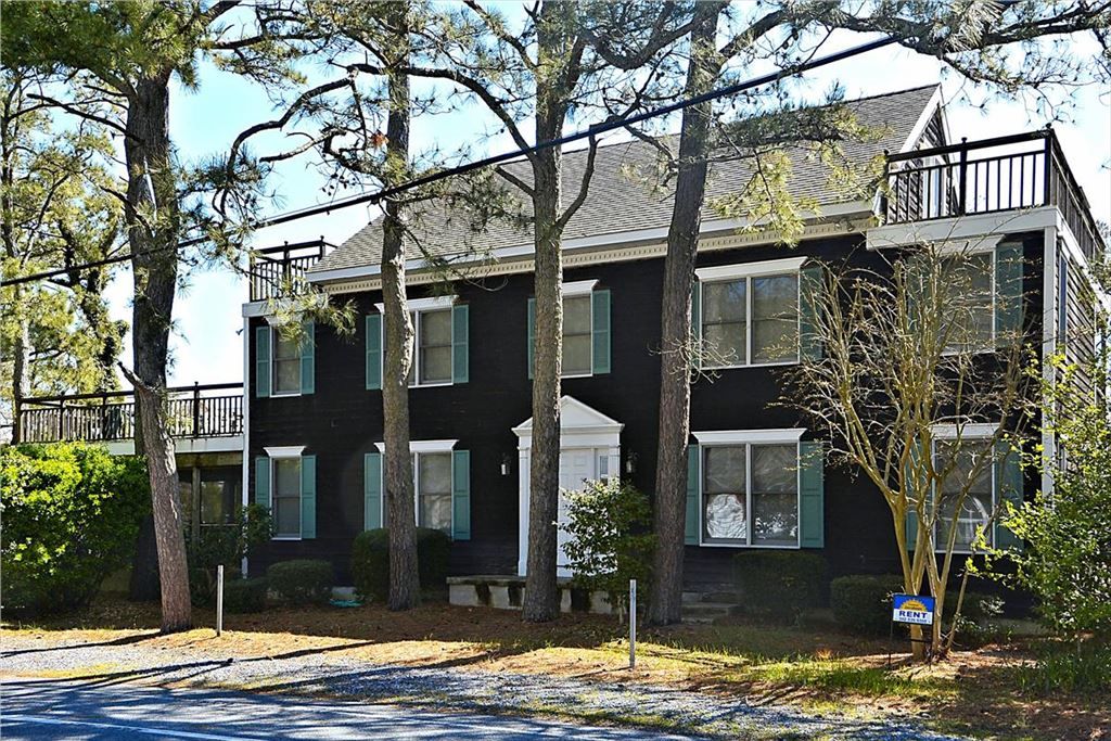 image This striking two-story vacation home features a black exterior with multiple windows framed by green shutters and a welcoming front porch flanked by tall trees.