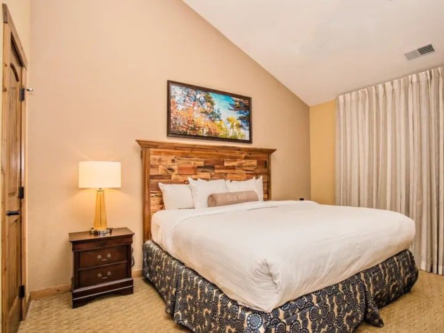 image Bedroom with king bed, warm lighting, and large window with curtains.