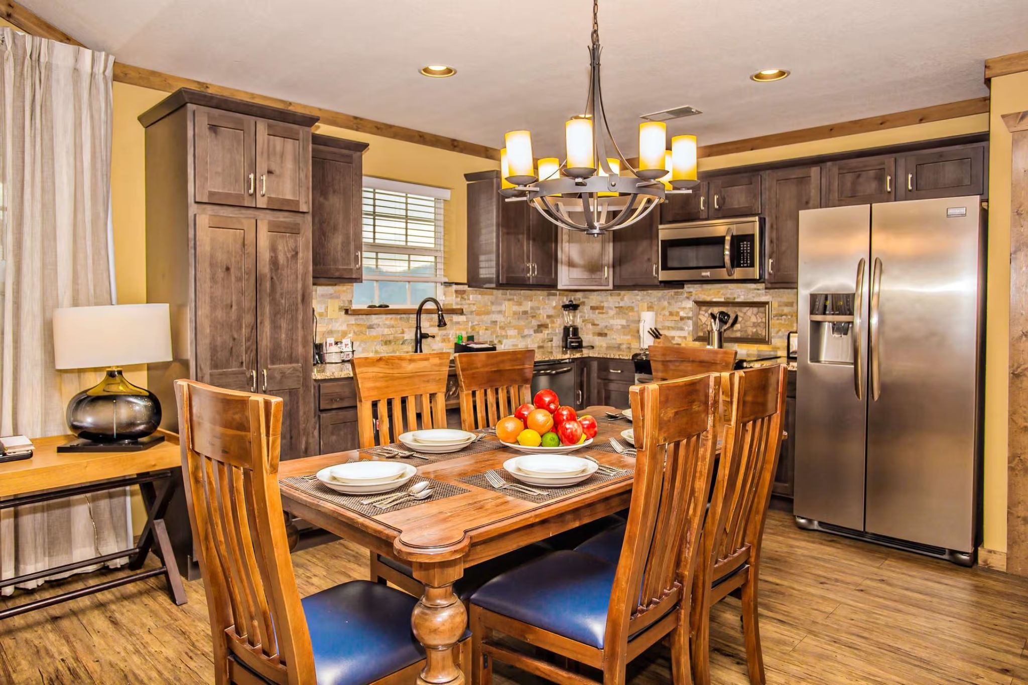 image Dining area with wooden table, chandelier, and adjacent full kitchen.