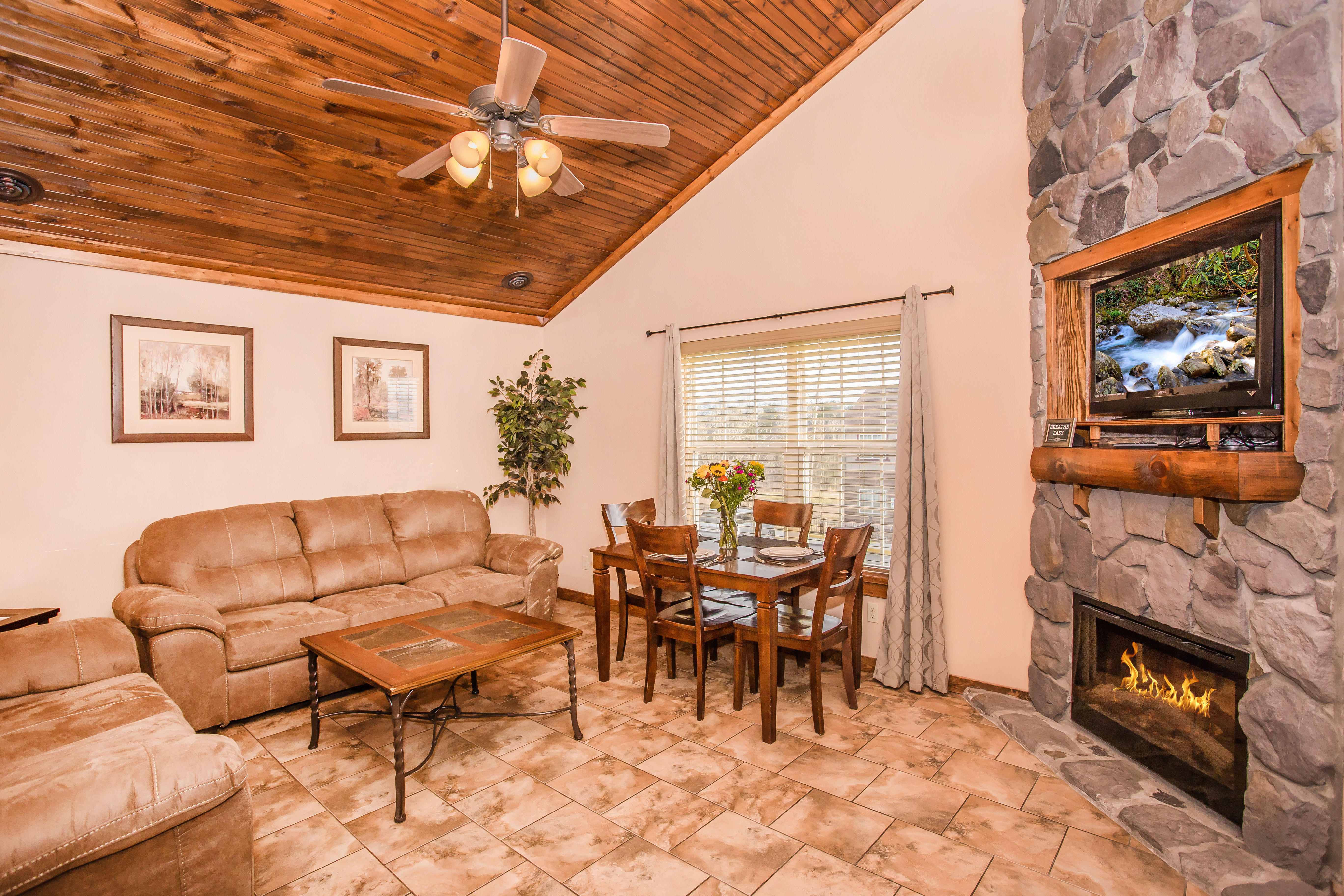 image Living room with sofa seating, stone fireplace, and vaulted wood ceiling.