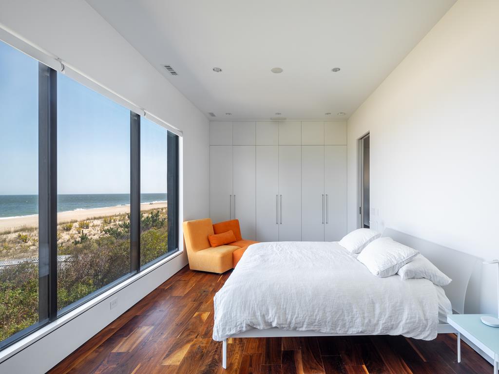 image This spacious bedroom features a plush bed, bright orange chair, and floor-to-ceiling windows that showcase stunning ocean views.