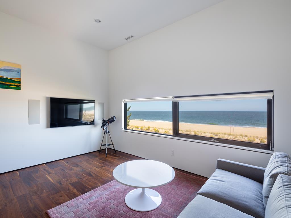 image A cozy sitting room awaits, complete with a plush sofa and telescope, all set against a backdrop of expansive ocean views from large windows.