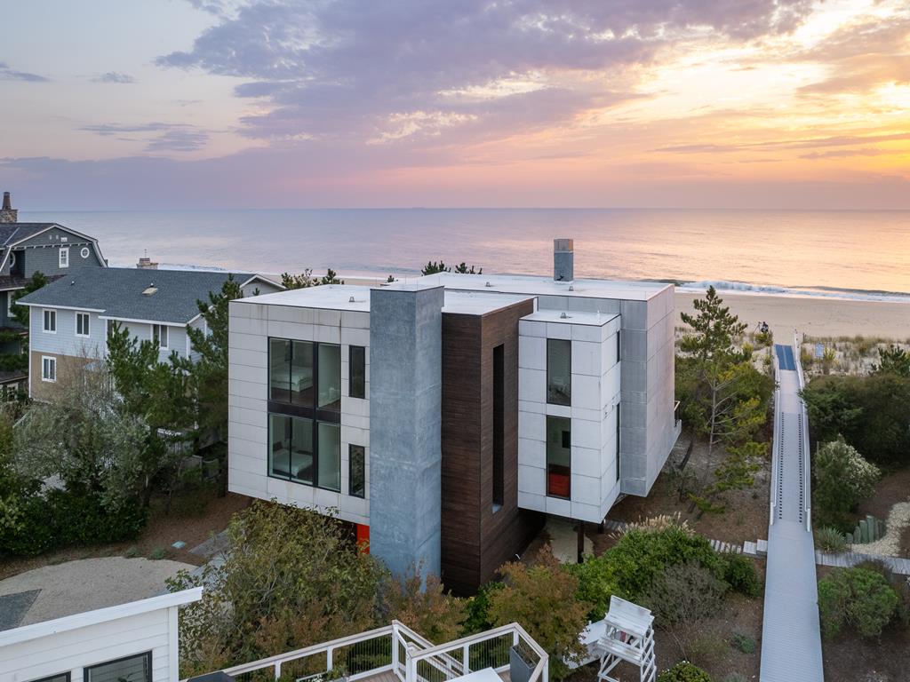 image The striking exterior of a modern beachfront home against a vibrant sunset, showcasing its sleek architecture and ocean access.