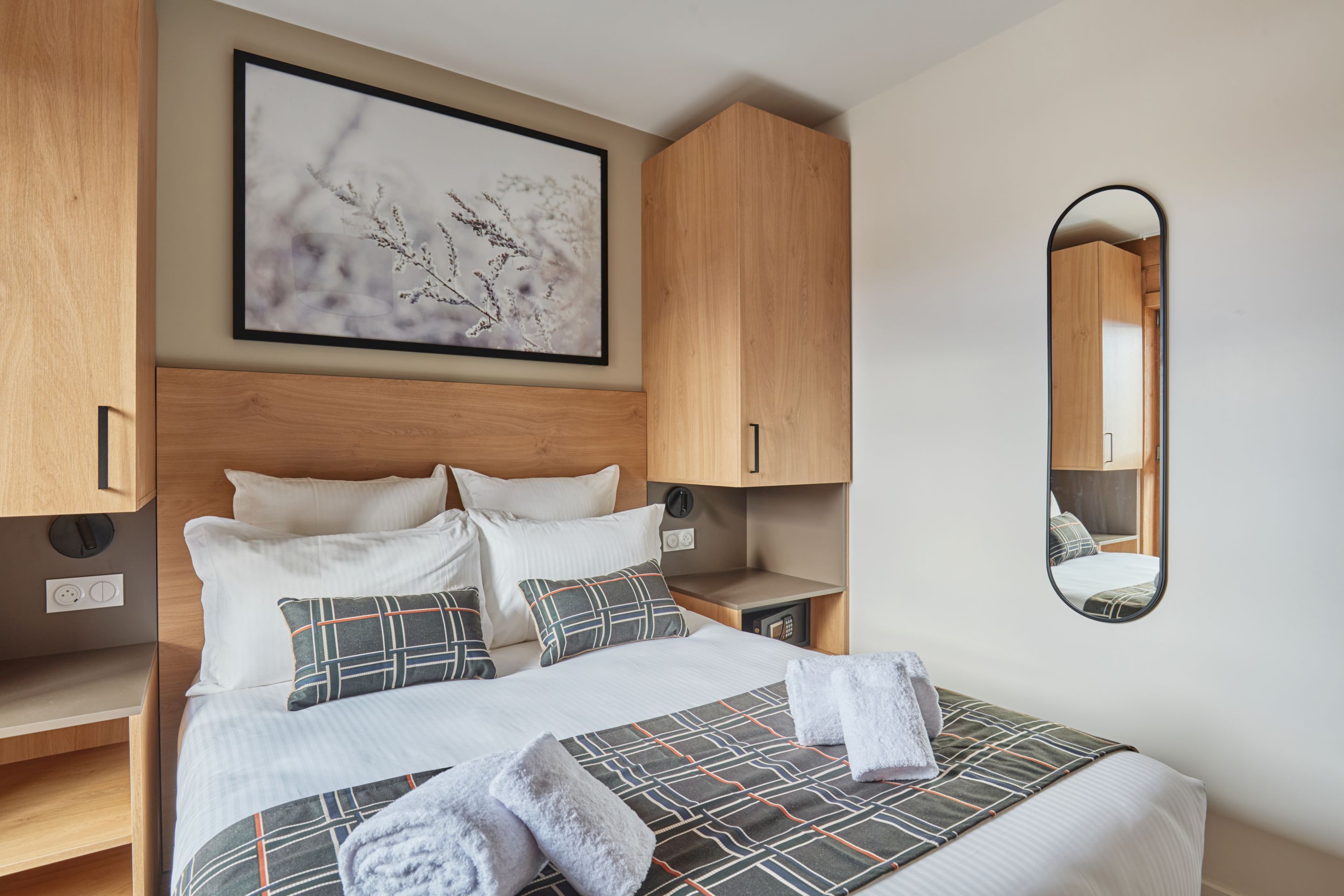 image Bedroom with a double bed, white linens, patterned pillows, wooden headboard, and a wall-mounted mirror above the cabinetry.