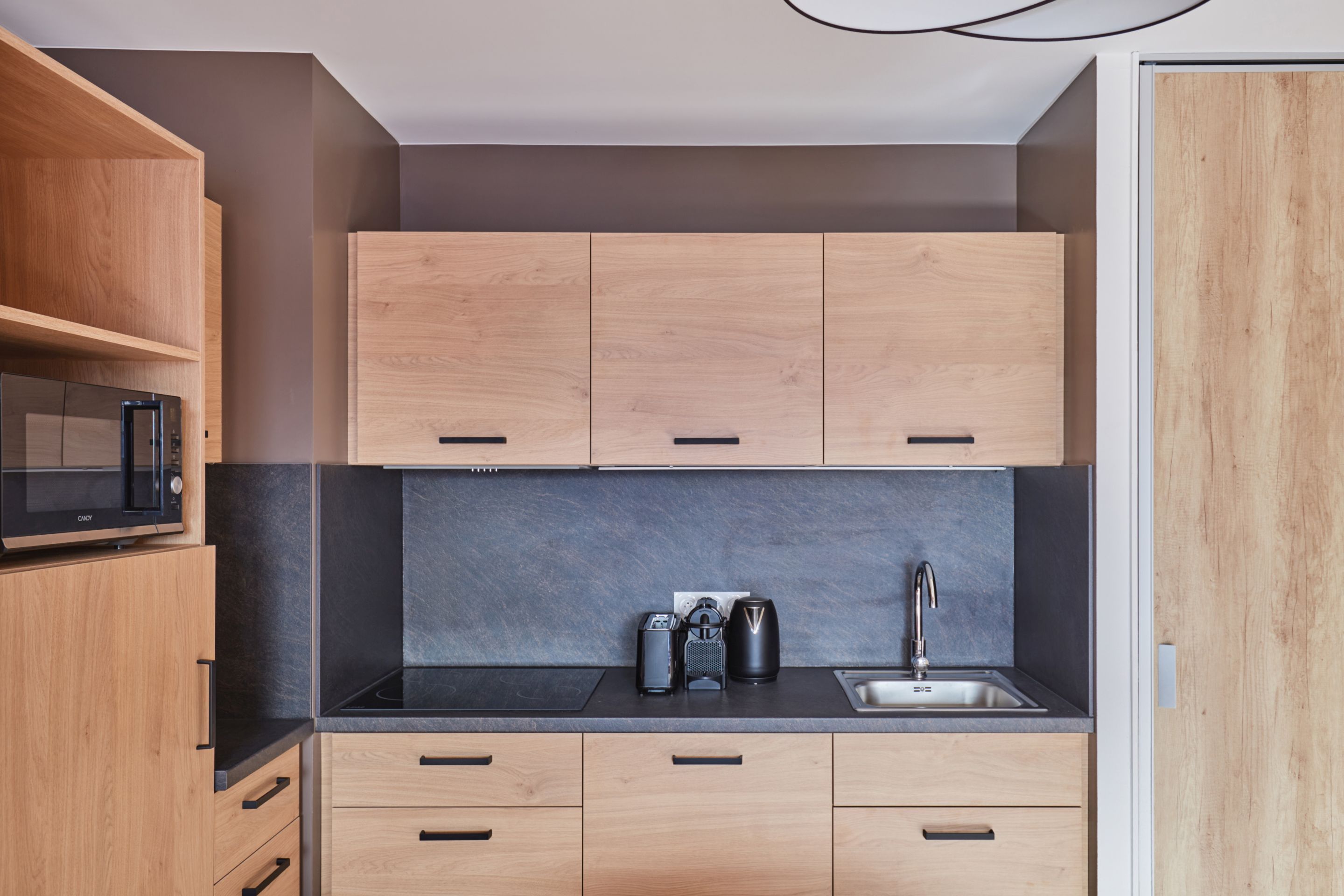 image Kitchenette close-up with light wood cabinets, microwave, coffee maker, kettle, and a dark slate back panel — fully equipped.