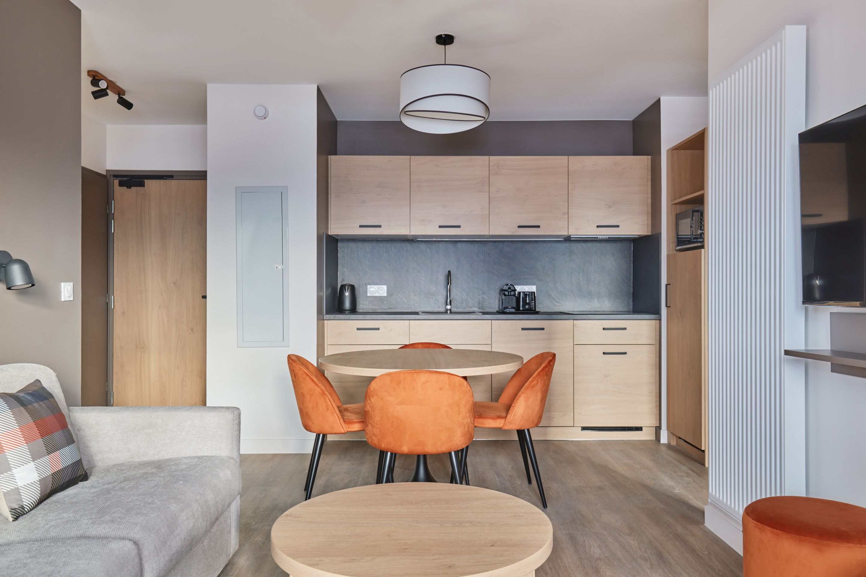 image Kitchenette with light cabinets, dark countertop, coffee maker, and kettle — the sofa with plaid cushions is visible in the background.