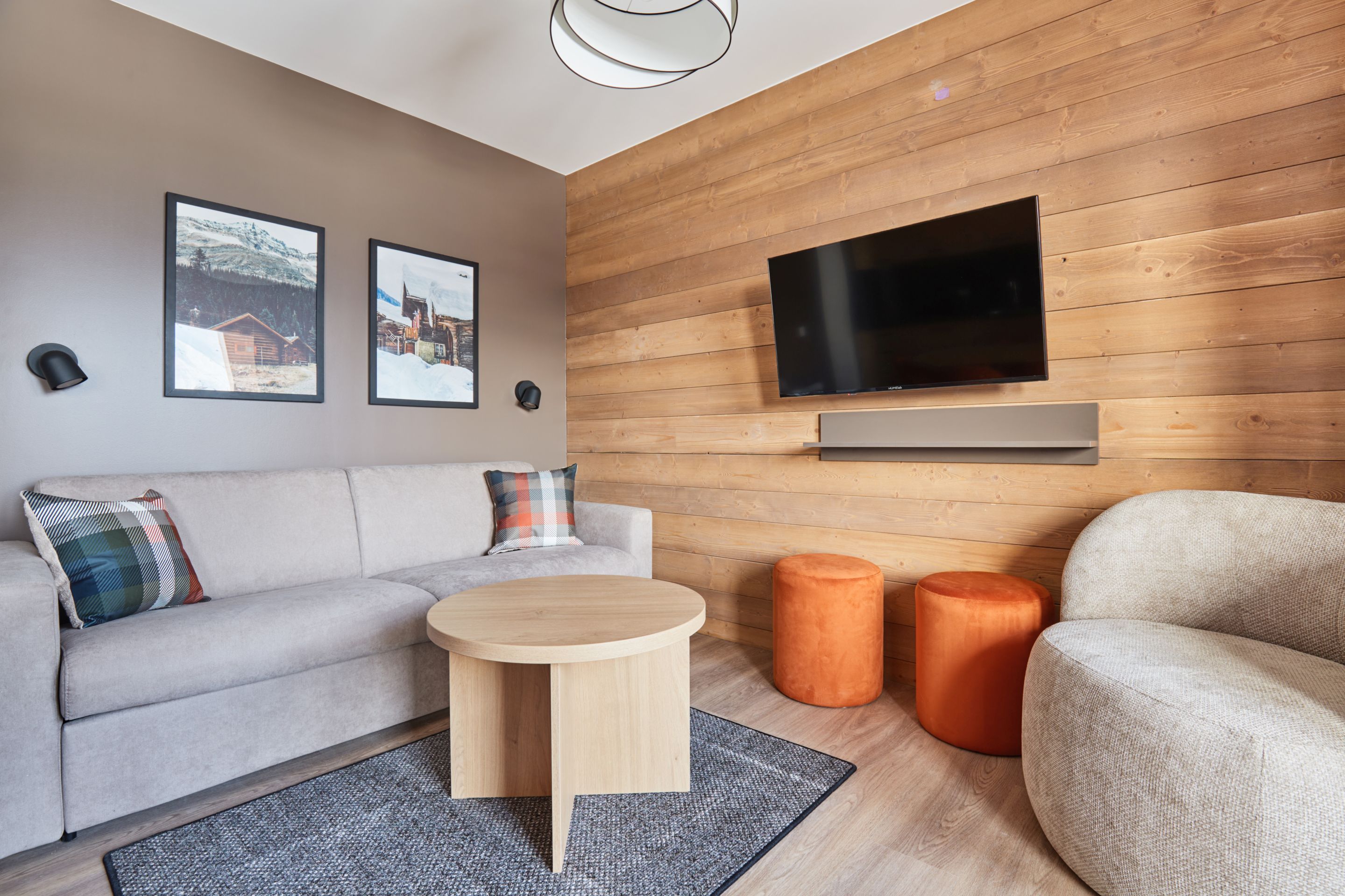 image Living area with a grey sofa, plaid cushions, round coffee table, and a TV mounted above the shelving unit.