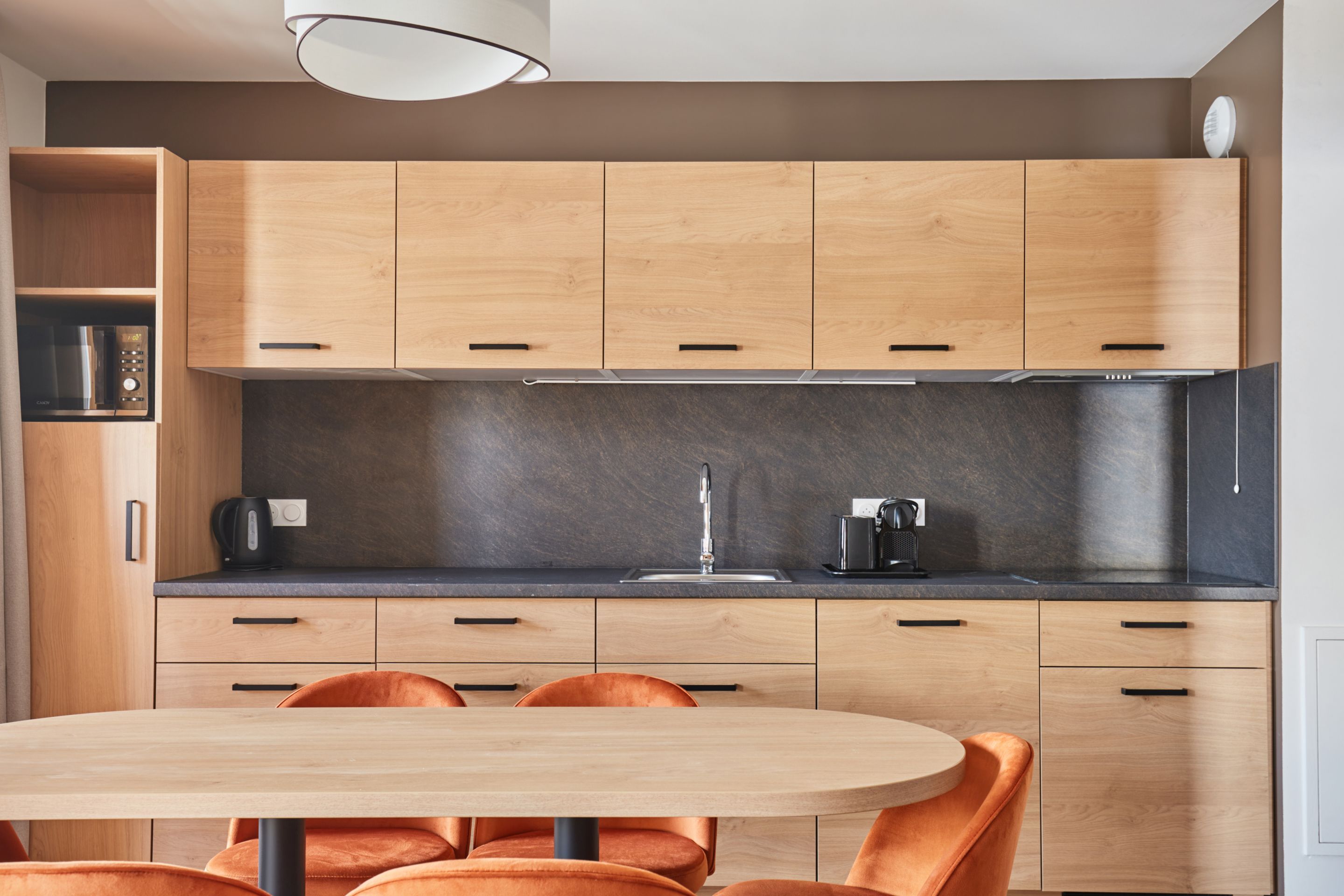 image Kitchenette with light wood cabinets, black countertop, microwave, kettle, and a sink — stovetop and dishwasher included.