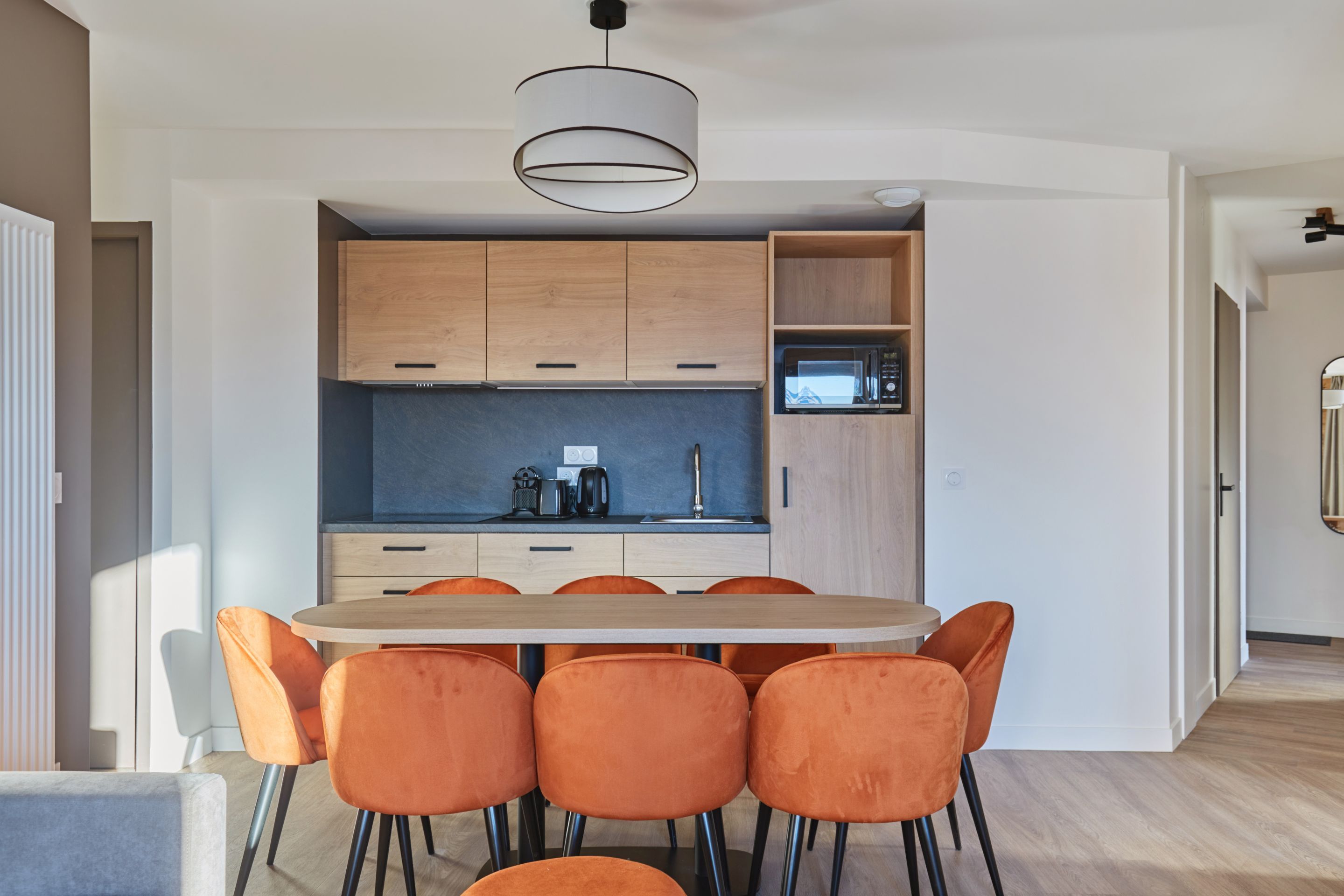 image Kitchenette with light wood cabinets, black countertop, microwave, and eight orange chairs around the dining table.