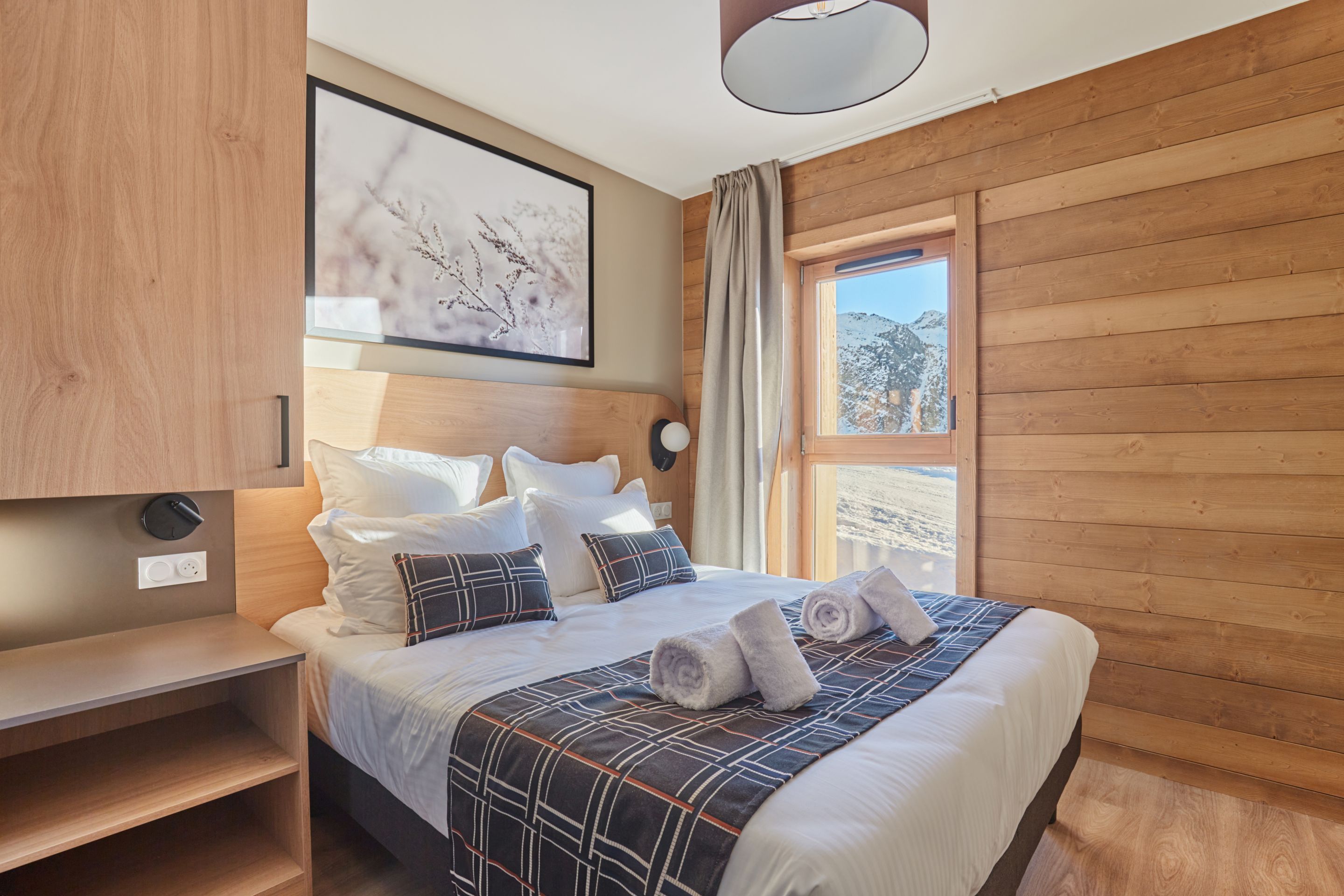 image Double bedroom with wood panelling, layered white linens, and a large window with a mountain view — bed linen included.