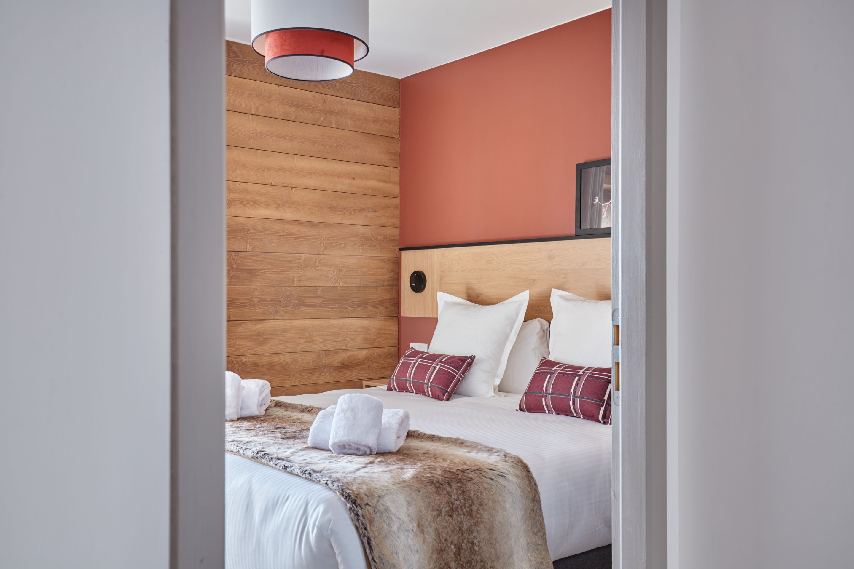 image Second double bedroom with matching terracotta tones, wooden accents, and rolled towels placed on the bed.