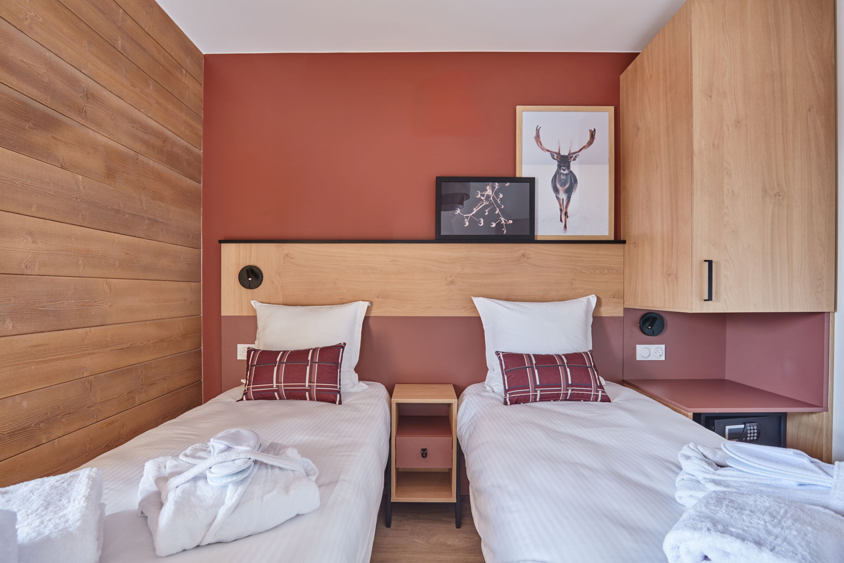 image Twin bedroom with two single beds, plaid cushions, and warm wood panelling on one wall.