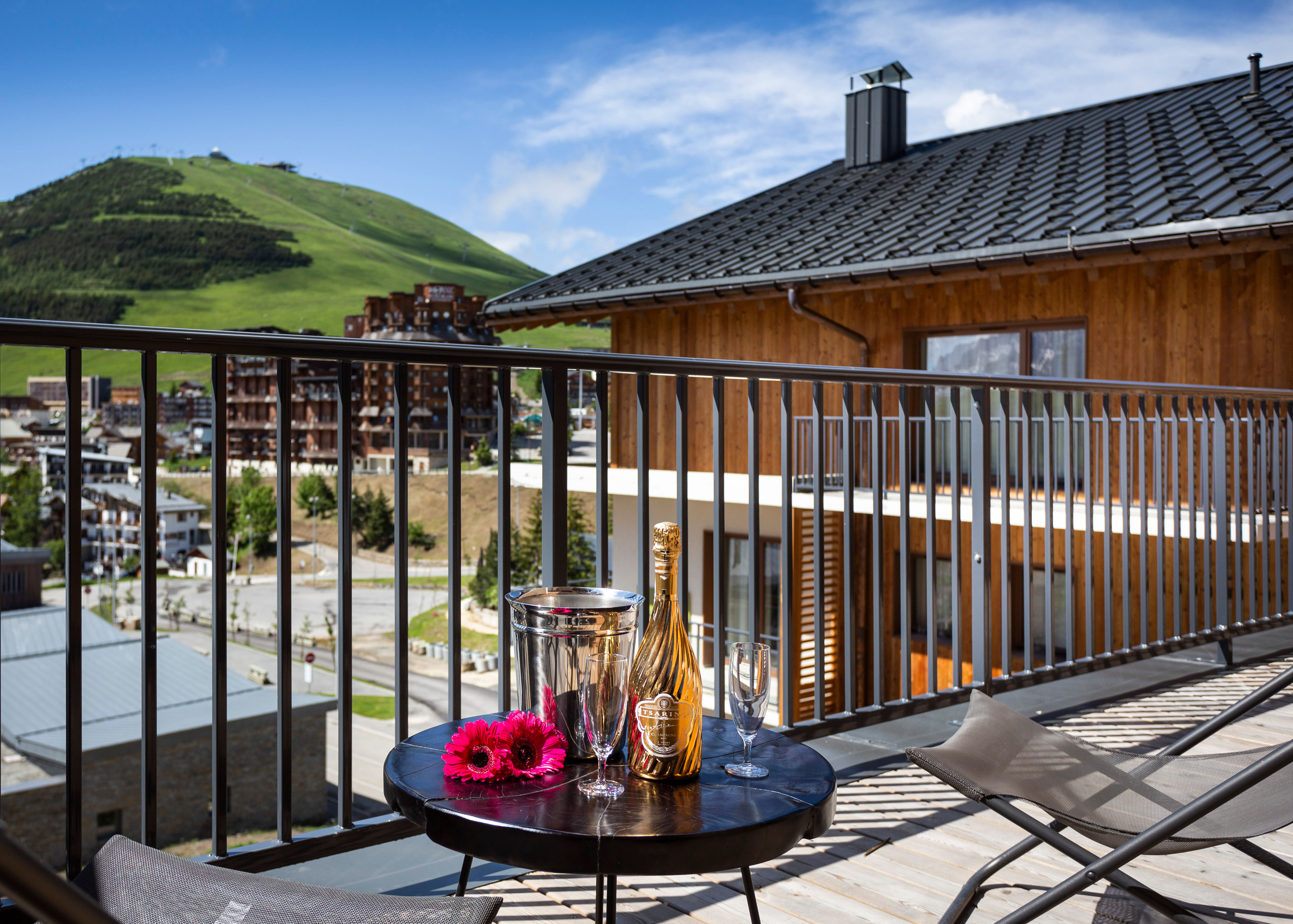 image An inviting balcony overlooks the stunning Alpe d’Huez landscape, featuring a table set with champagne and flowers, perfect for romantic outdoor moments.