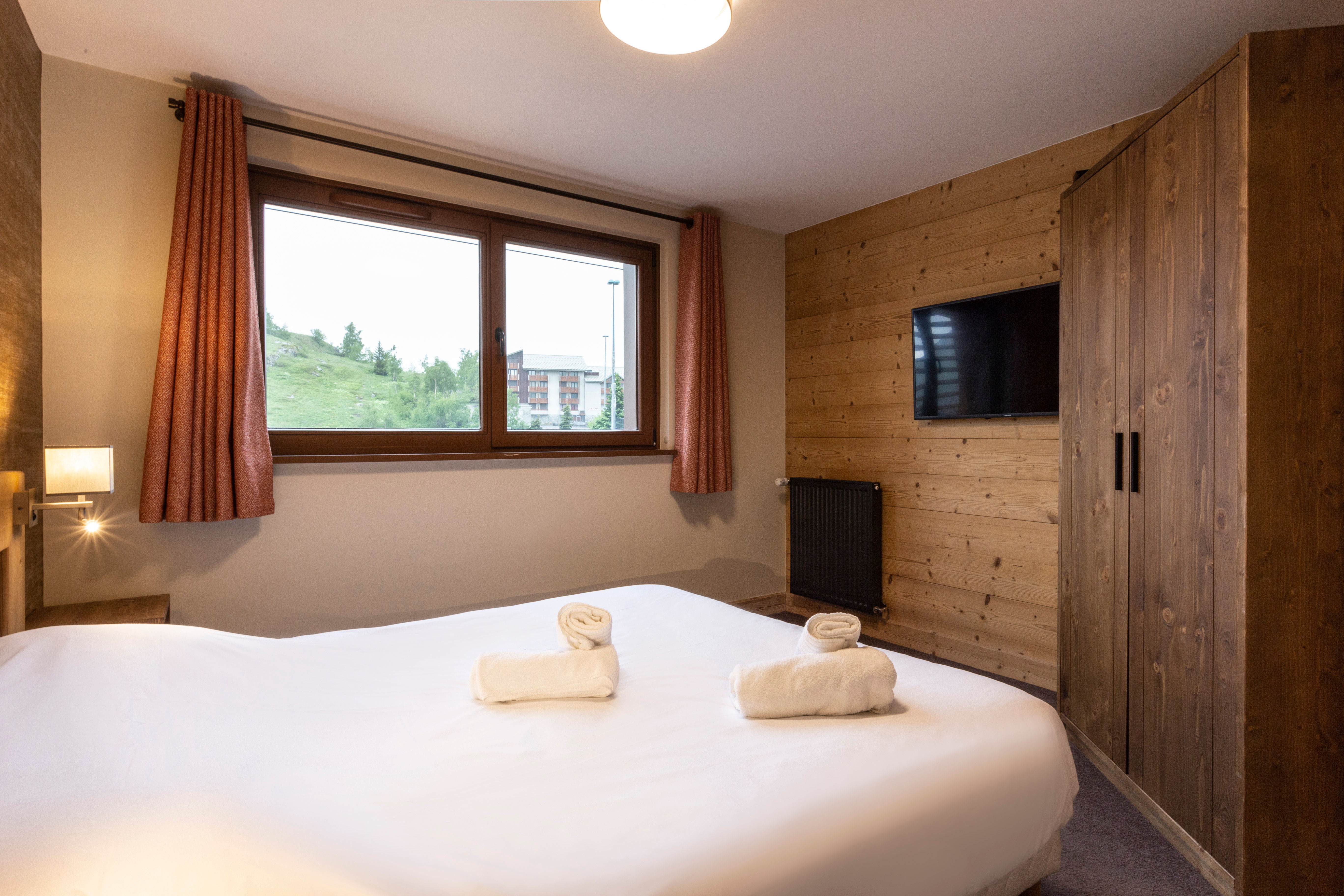 image Serene double bedroom with panoramic mountain views and warm wood tones for a peaceful Alpine escape.