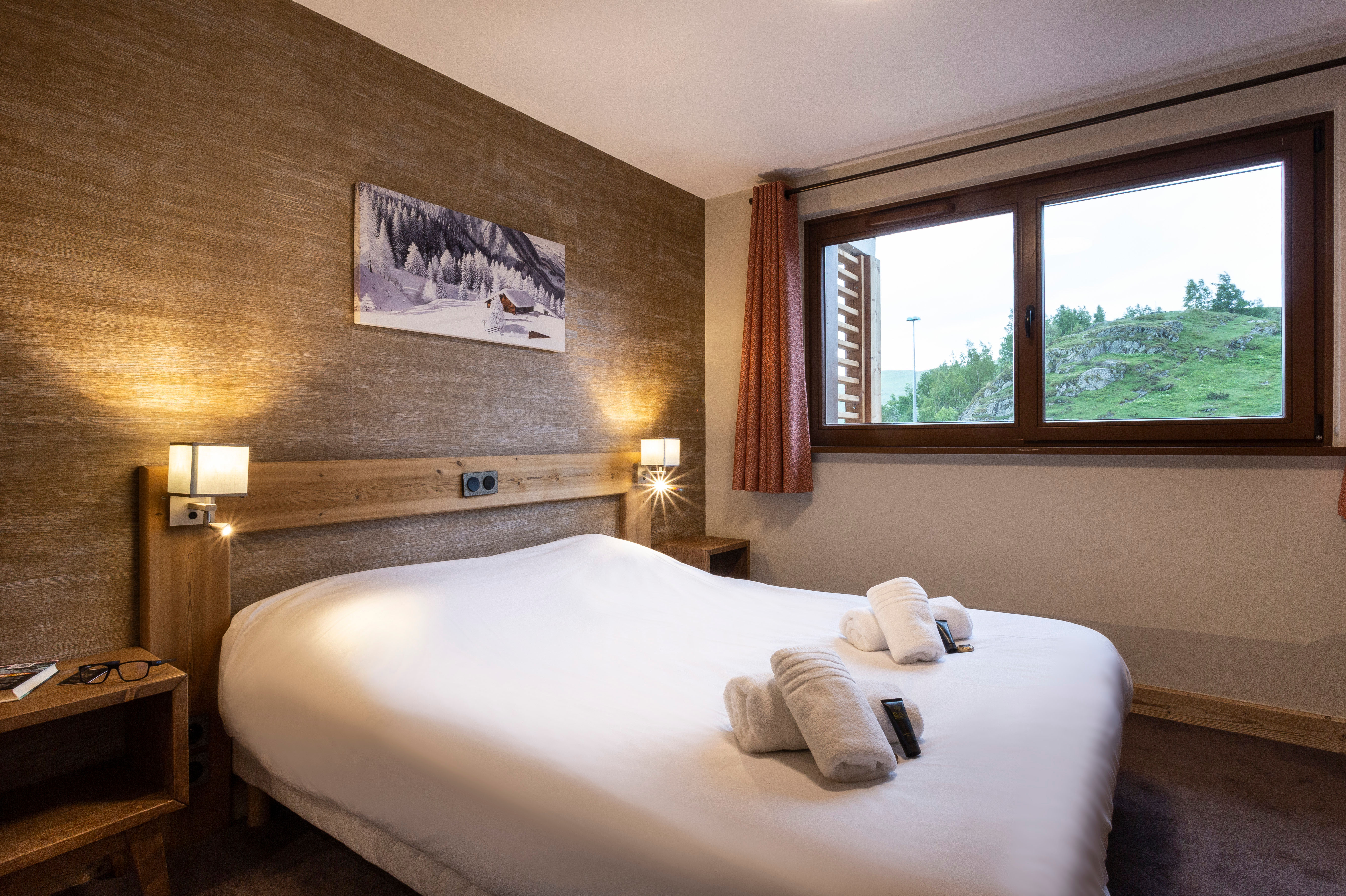 image Bright and serene bedroom with alpine artwork and scenic mountain views through oversized windows.