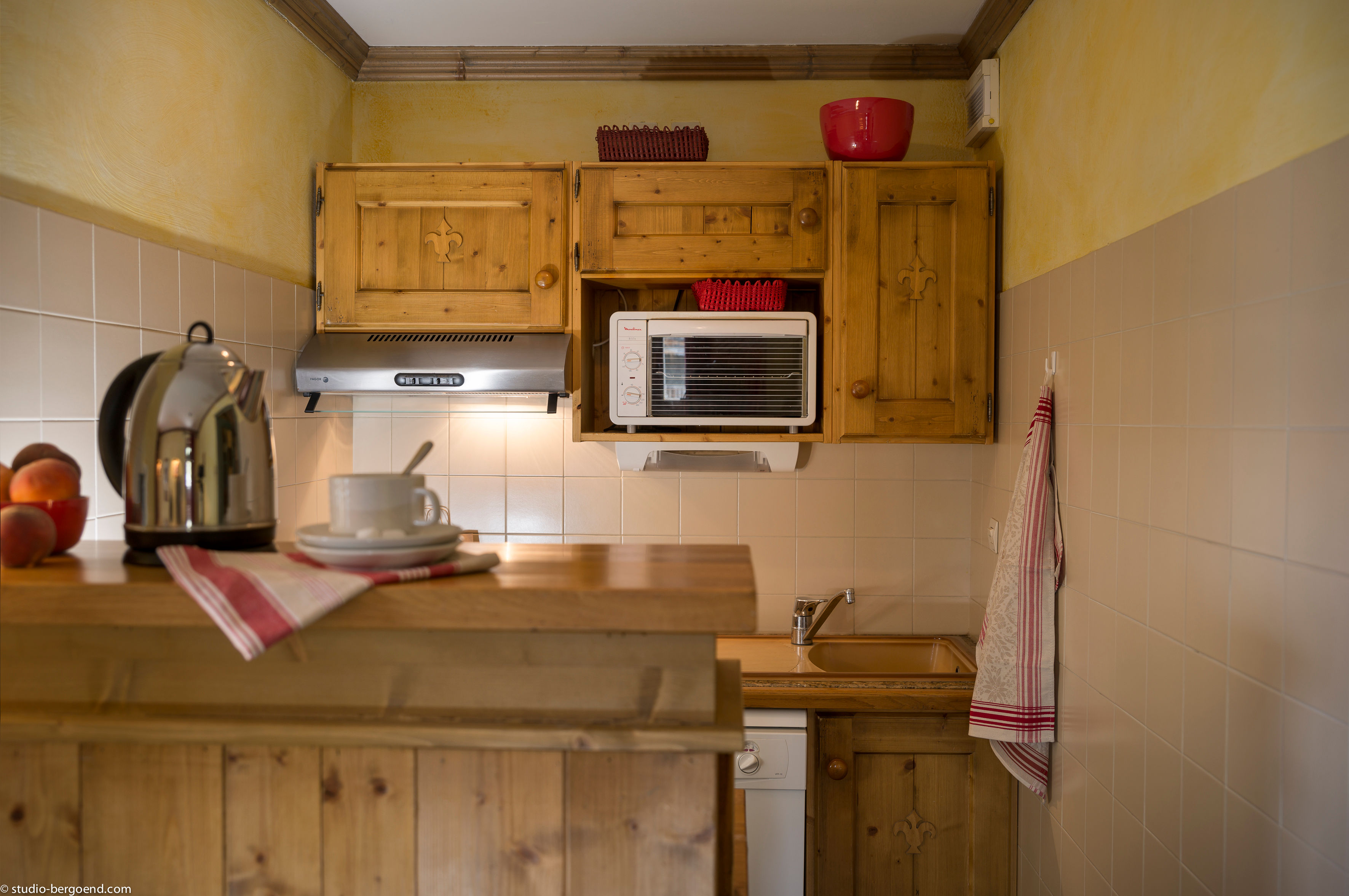 image Compact kitchen with wooden cabinets, sink, stove, and microwave — all you need for a self-catered stay