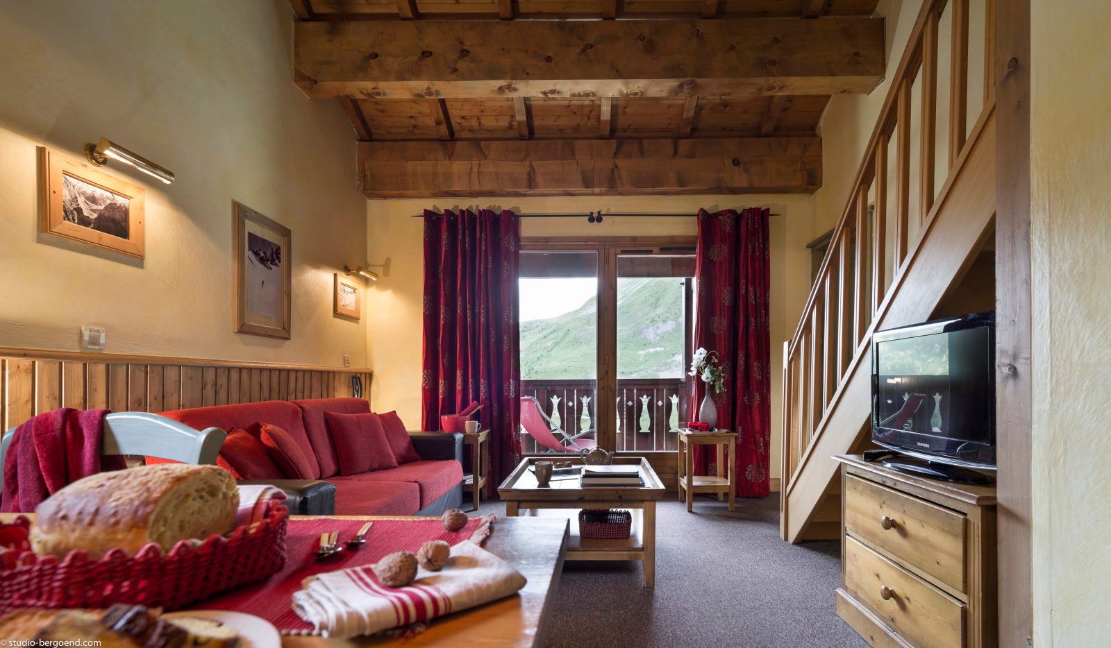 image Living room with red curtains, a sofa, large windows, and warm wooden decor