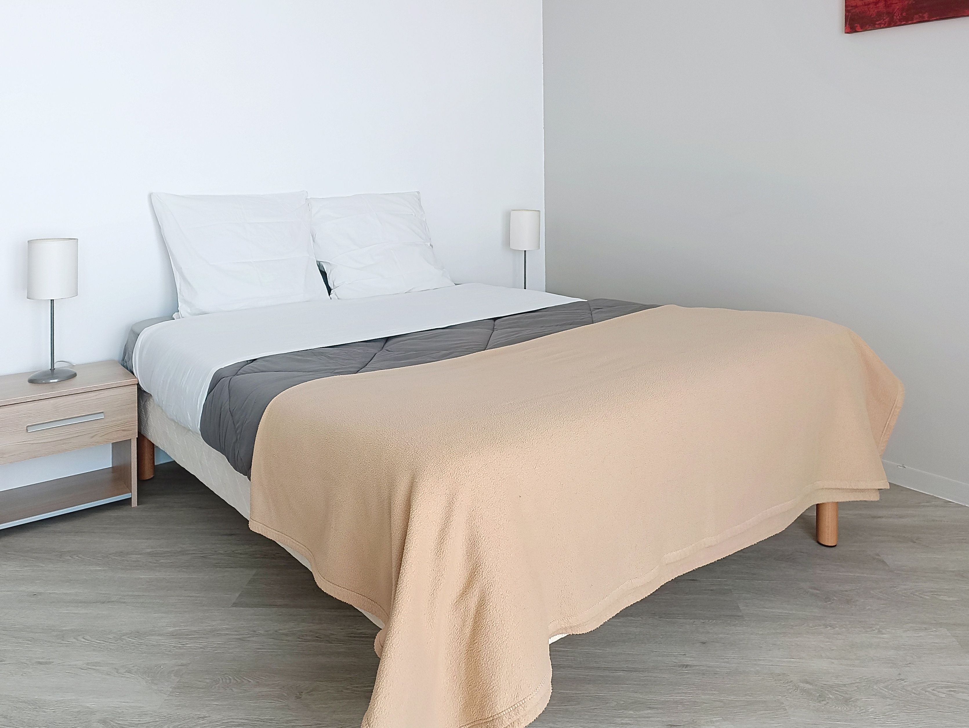 image Neatly made bed with beige blanket and pillows.