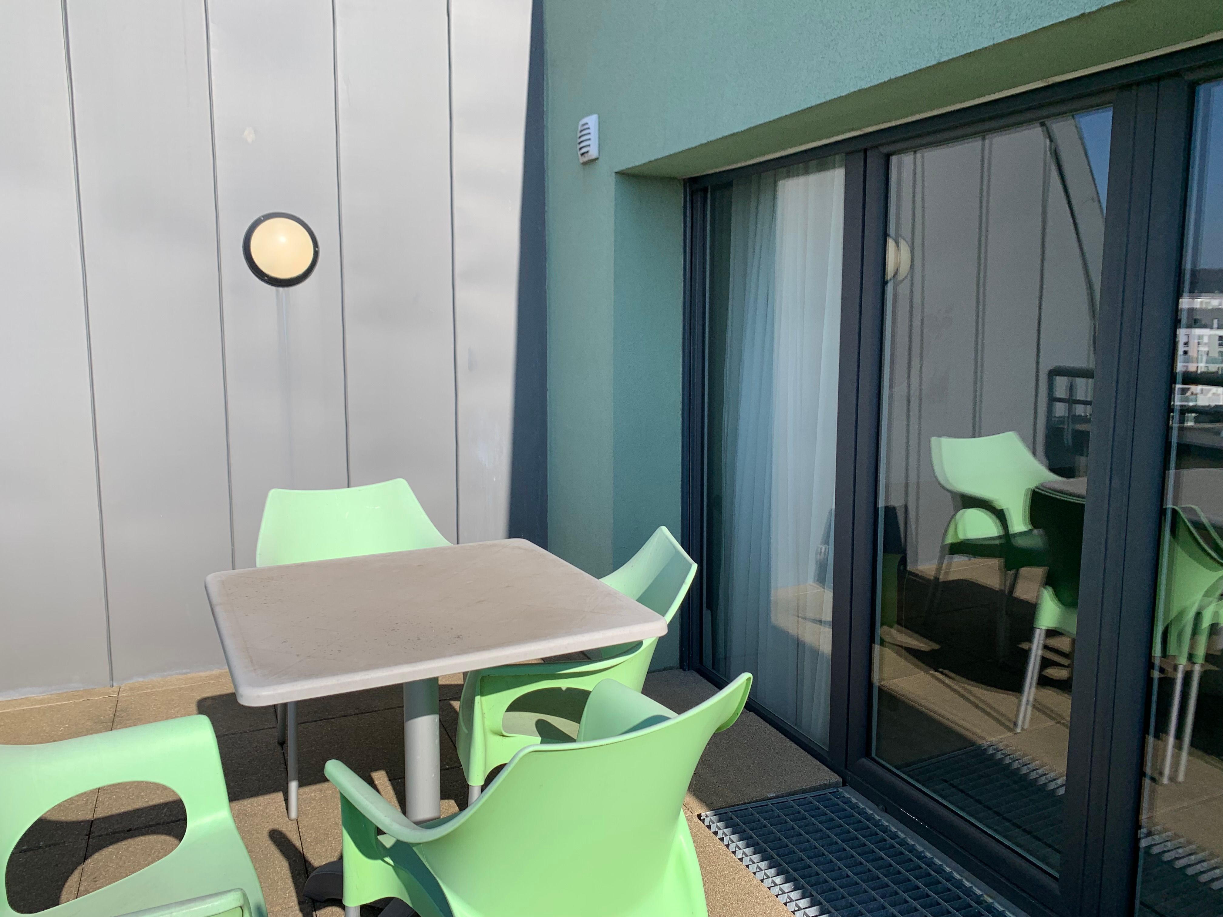 image Enjoy outdoor dining on the terrace with modern green chairs and a minimalist table, perfect for relaxing moments.