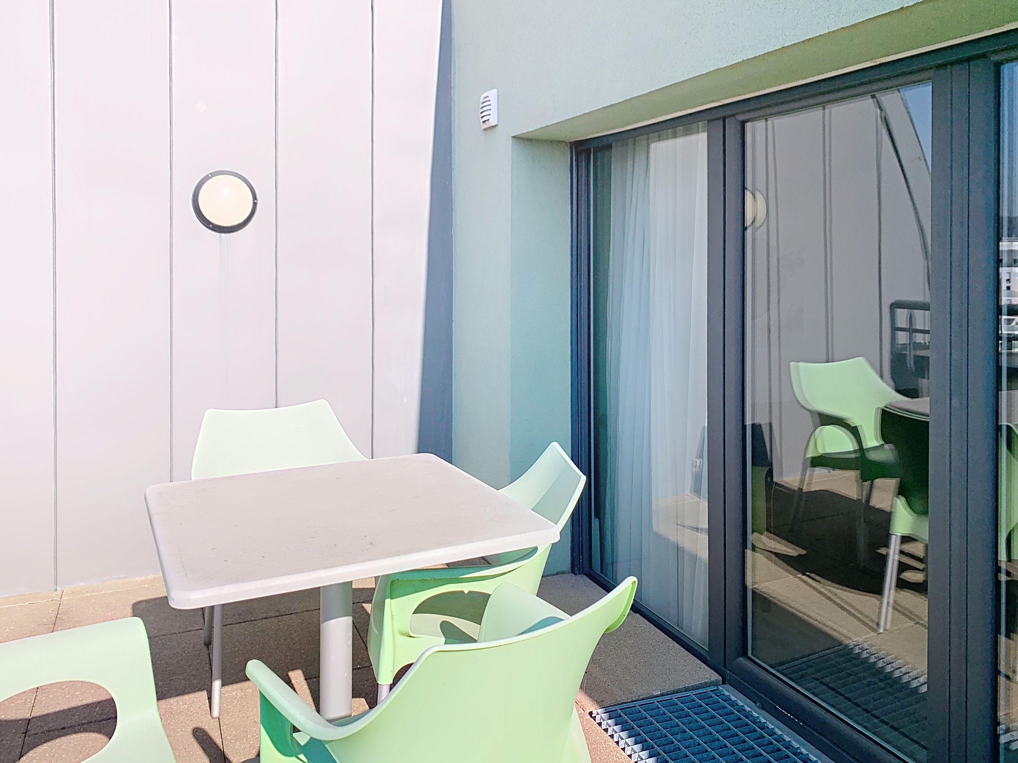image Enjoy outdoor dining on the terrace with modern green chairs and a minimalist table, perfect for relaxing moments.