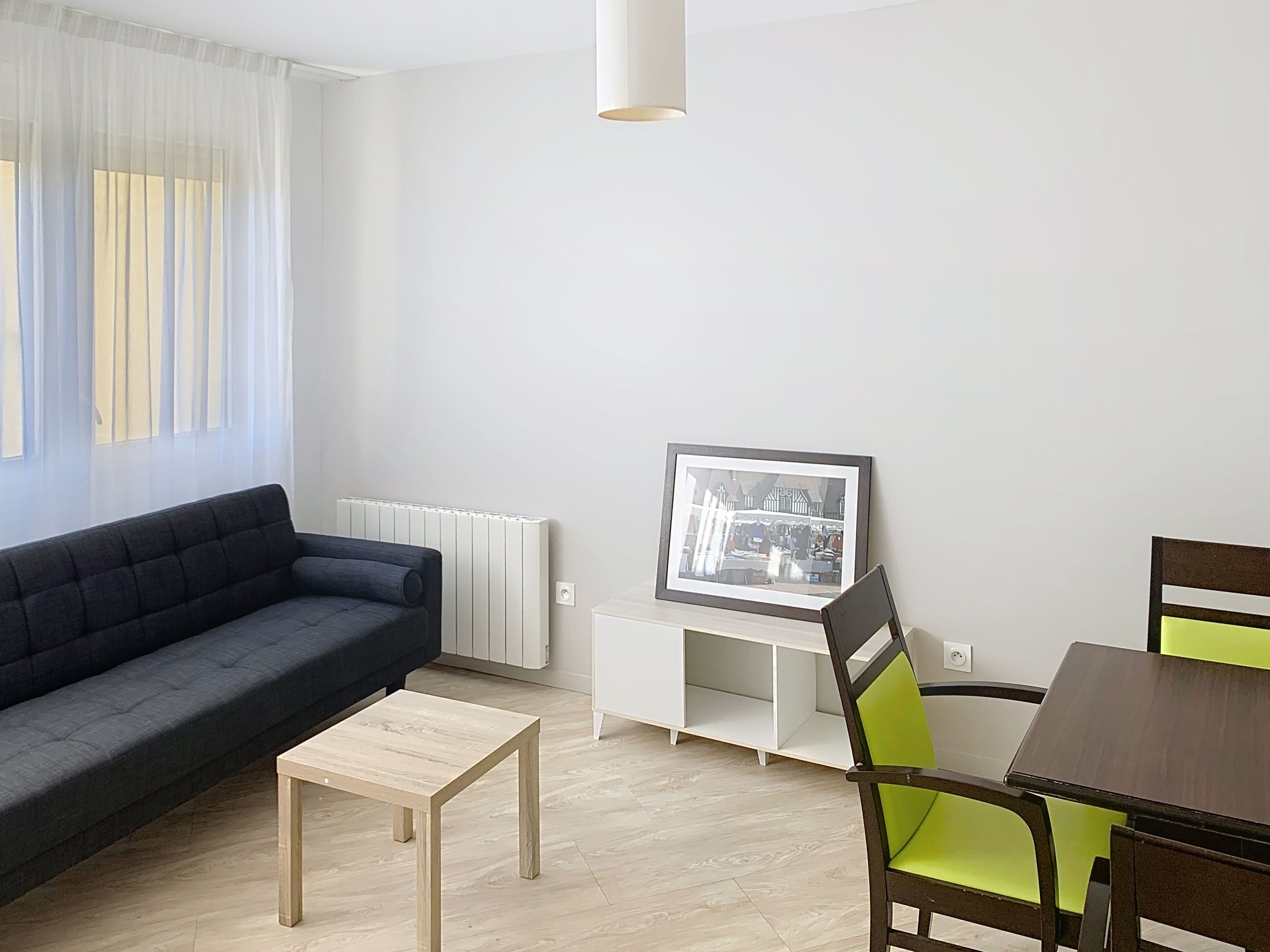 image Bright living and dining area featuring a sofa, dining table, and green chairs in this apartment.
