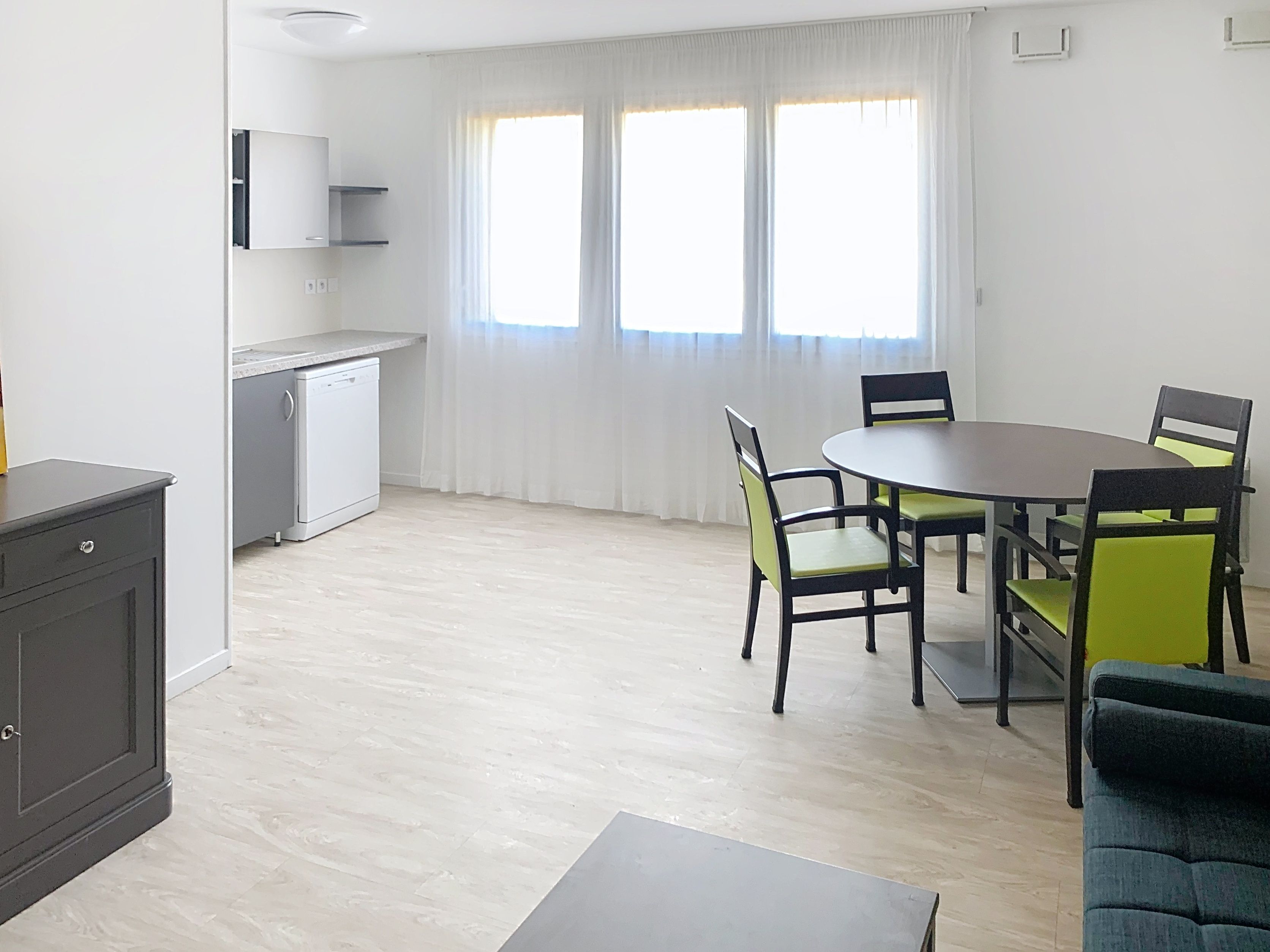 image Open plan living and dining space with green accent chairs and ample natural light.