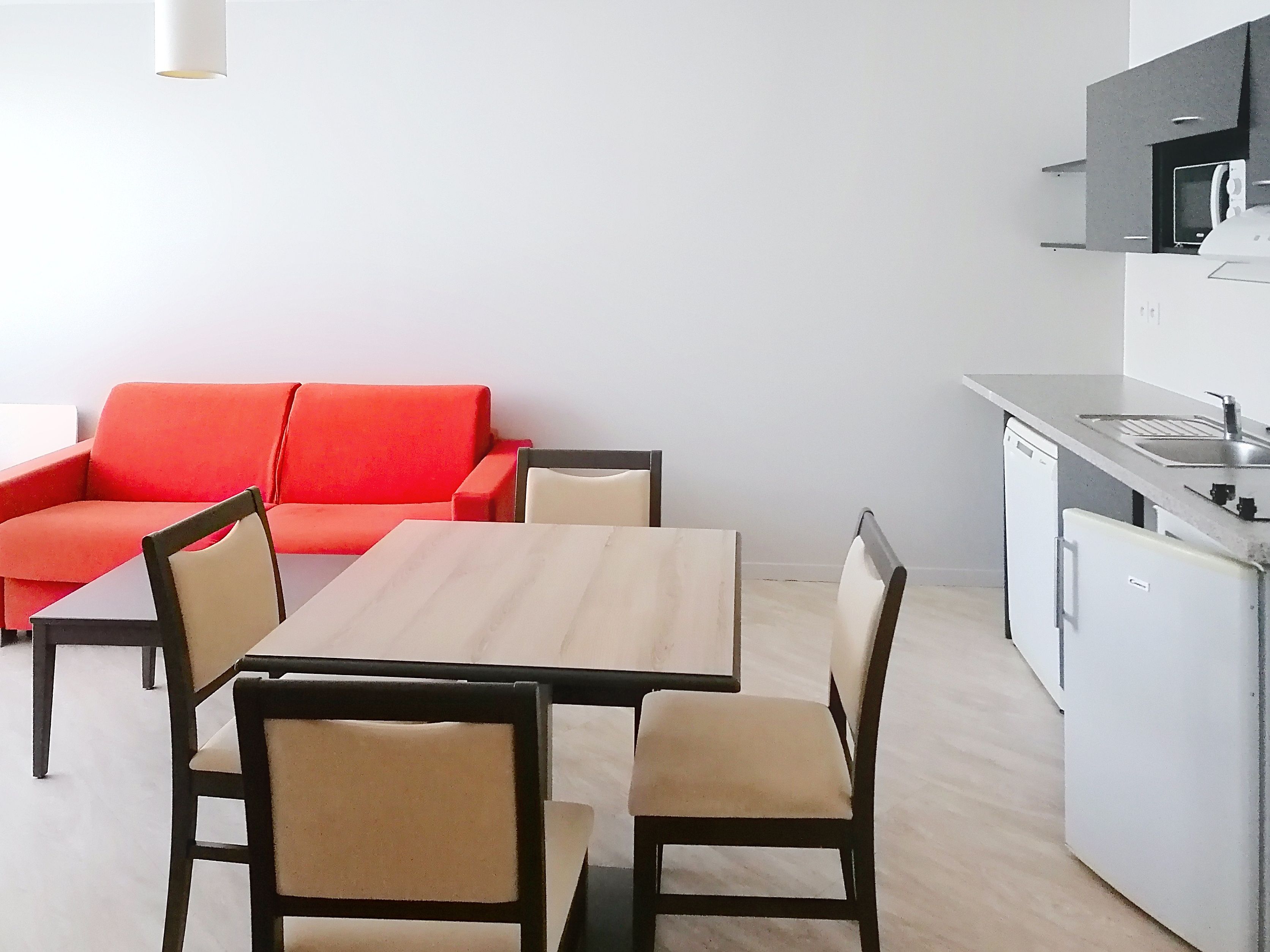 image Bright living and dining area featuring a red sofa and dining table with direct access to the kitchen.