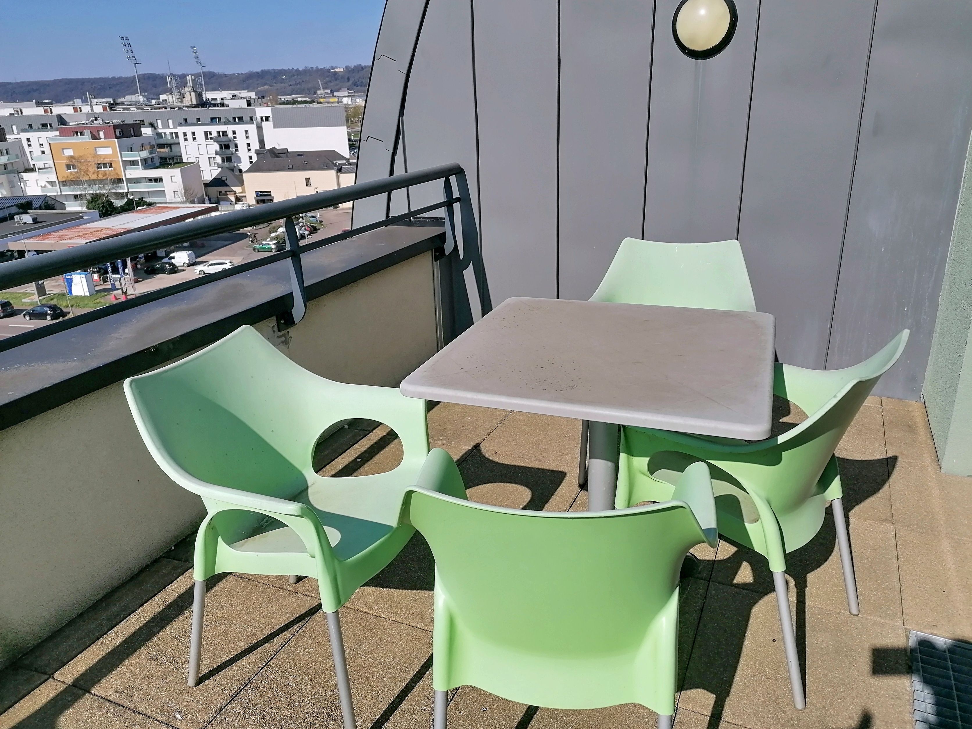 image Private furnished terrace with dining table and green chairs, offering views of the city.