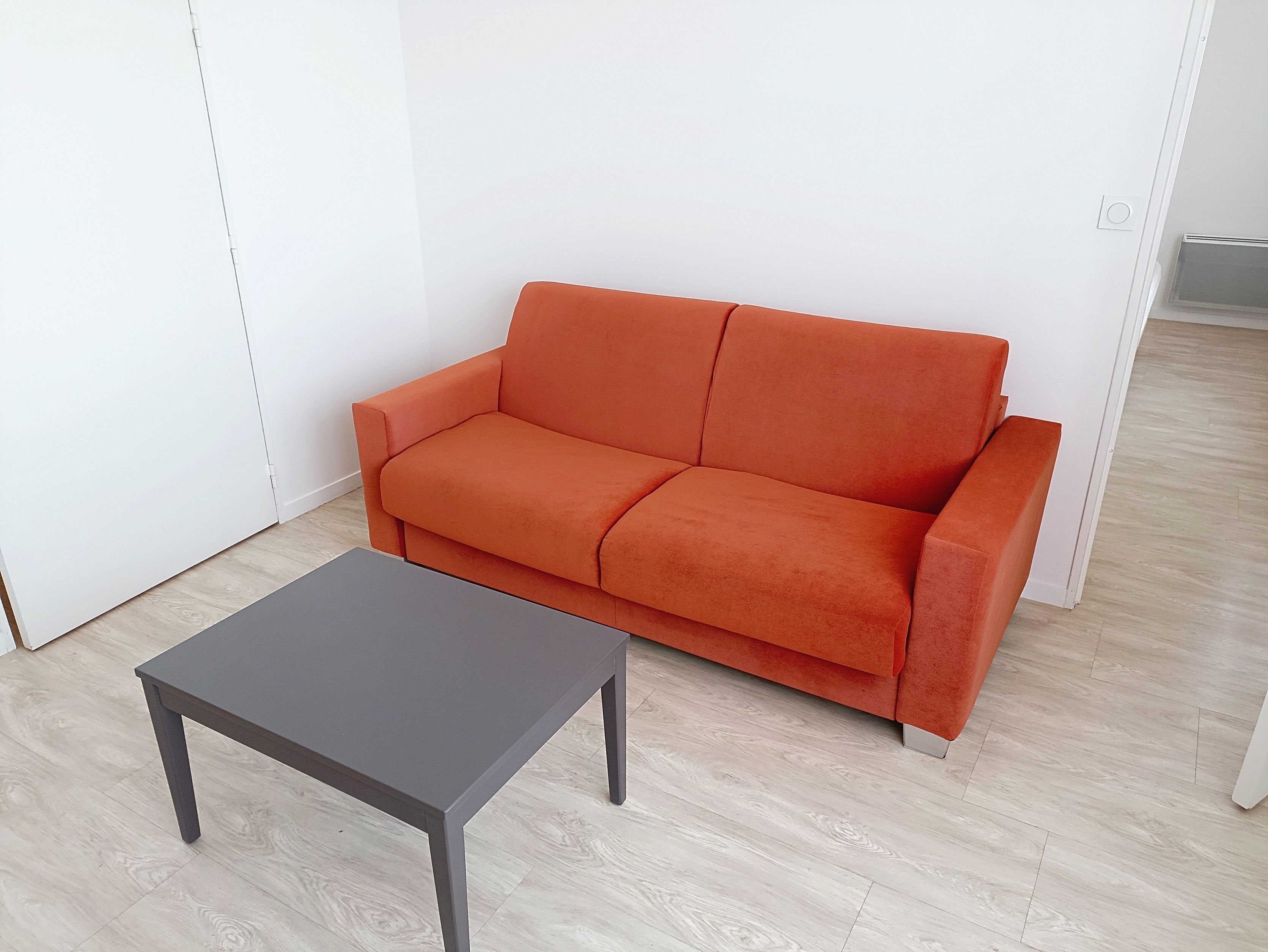 image Spacious living room with a red sofa, coffee table, and ample natural light.