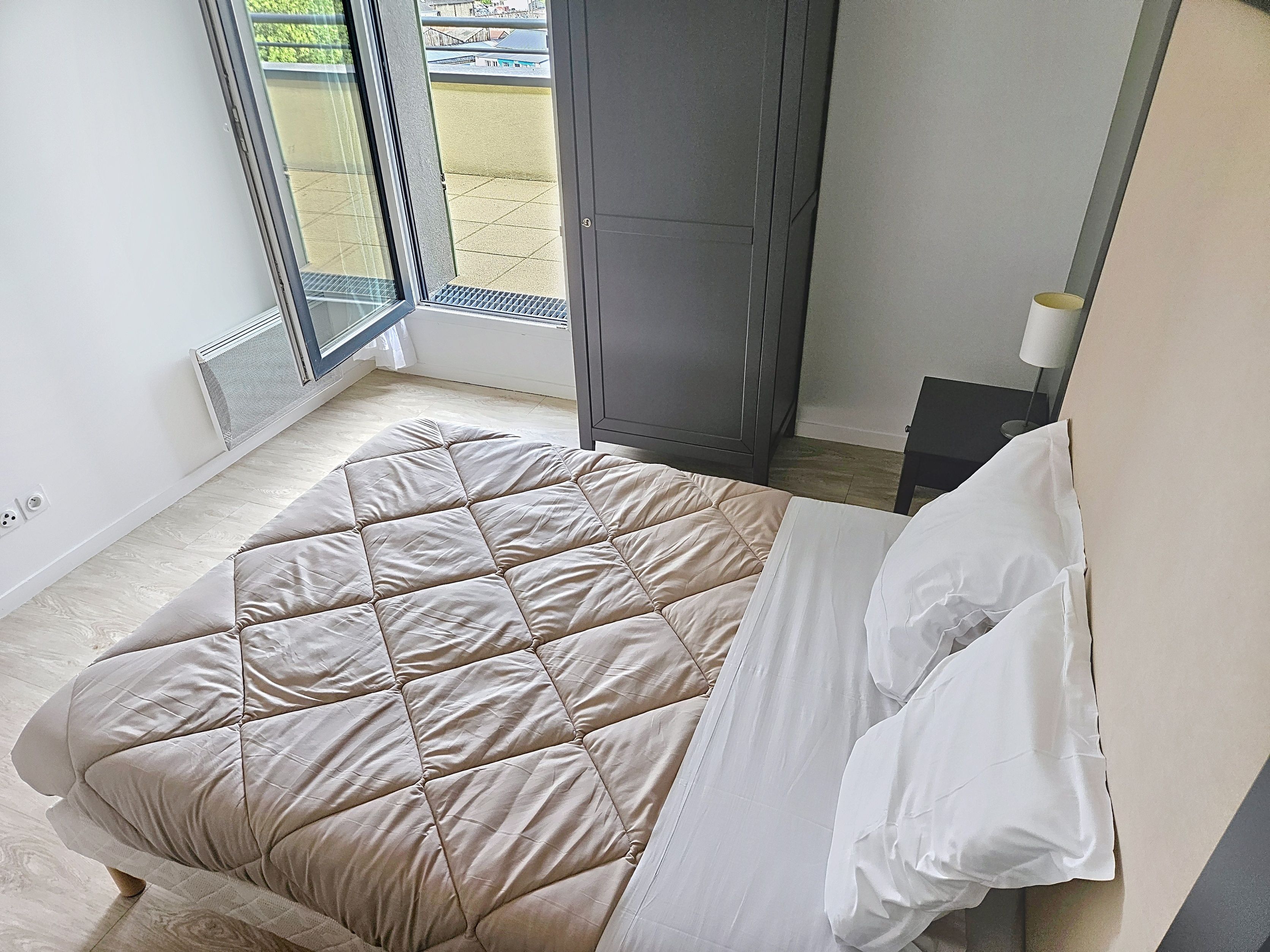 image Bed with quilted cover, bedside table, and open balcony door.