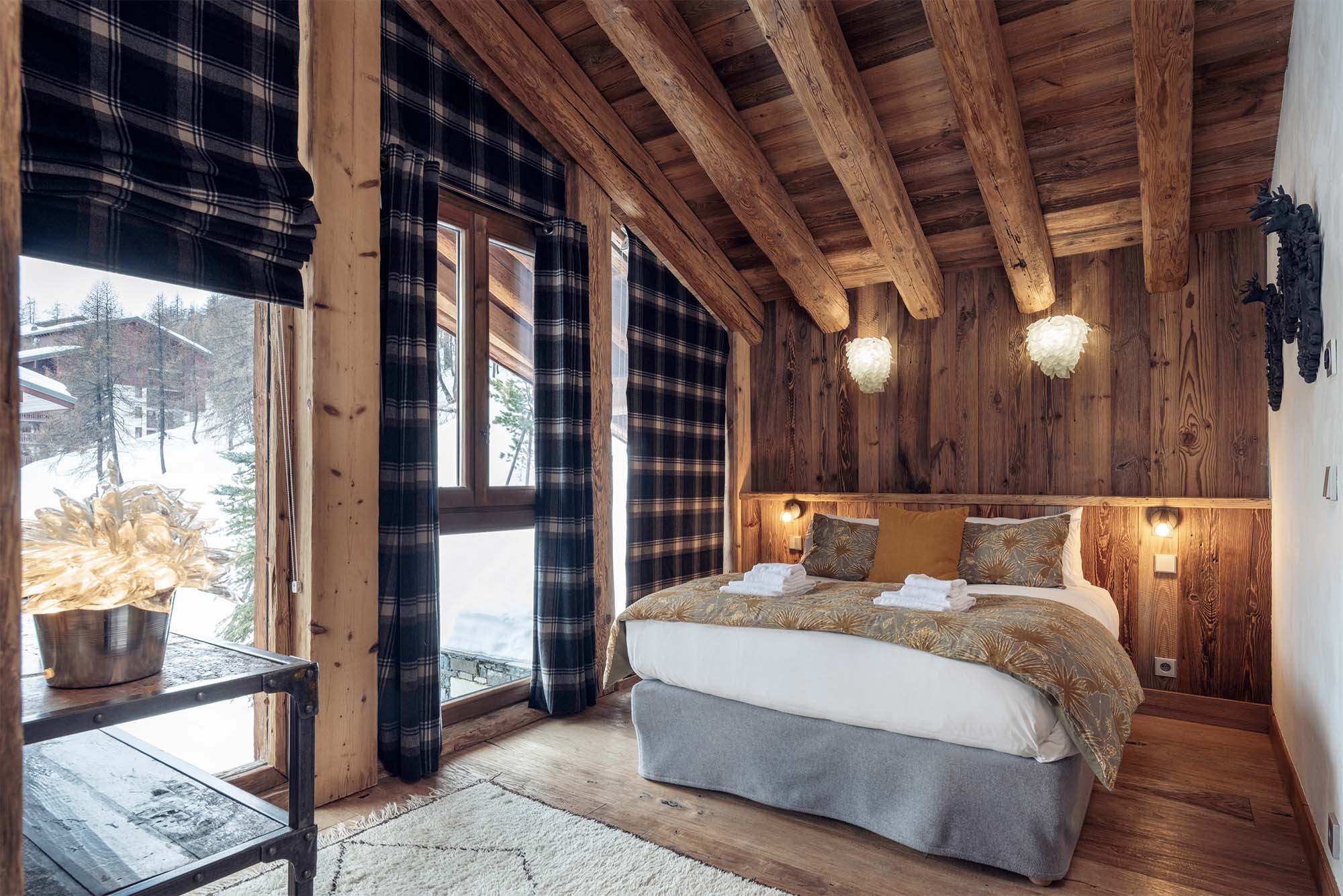 image Retreat to a beautifully appointed bedroom where bespoke décor, cozy textiles, and stunning views create a serene alpine sanctuary at Chalet Genepy.