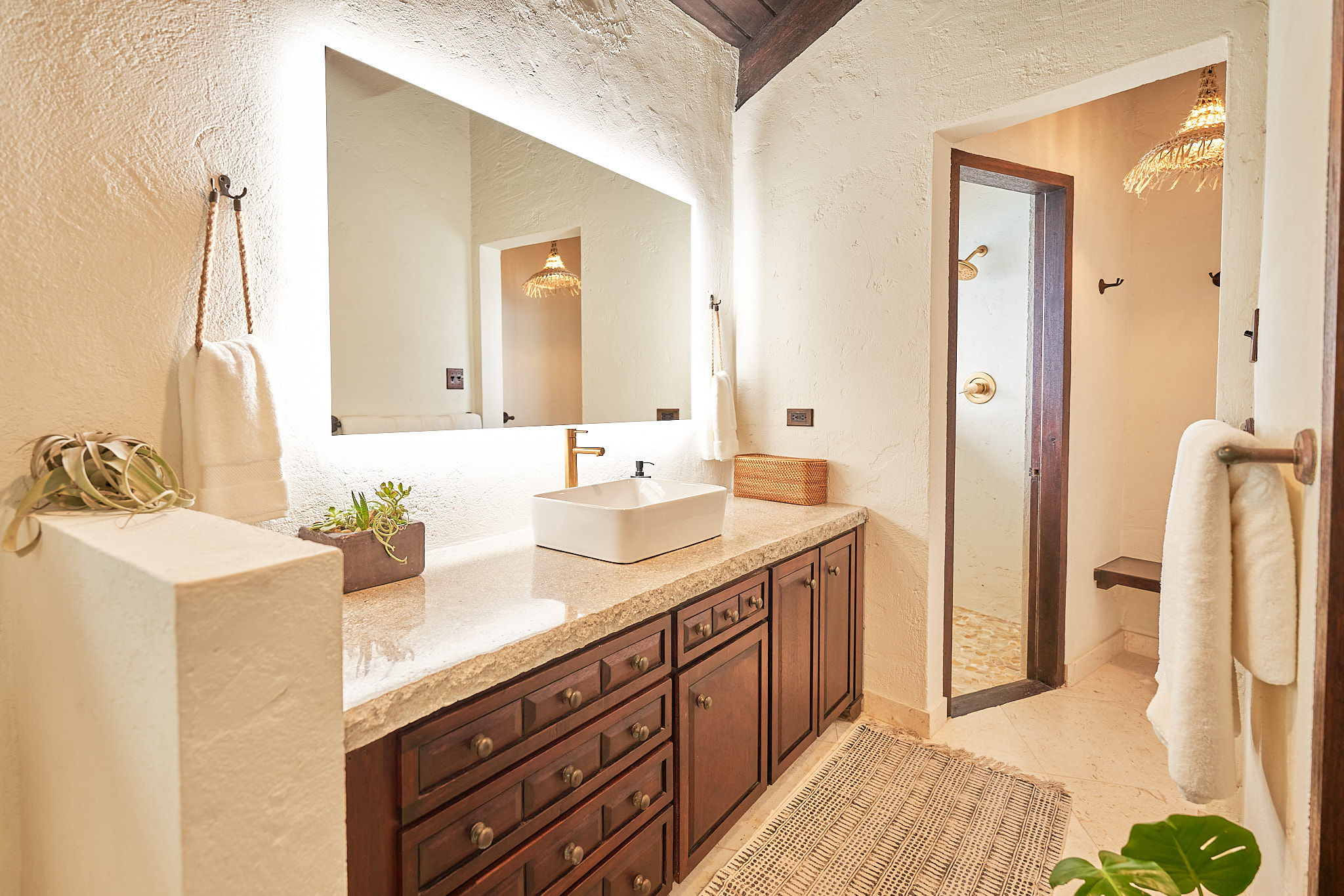 image Stylish bathroom with warm wood cabinetry, a modern vessel sink, backlit mirror, and a walk-in shower.