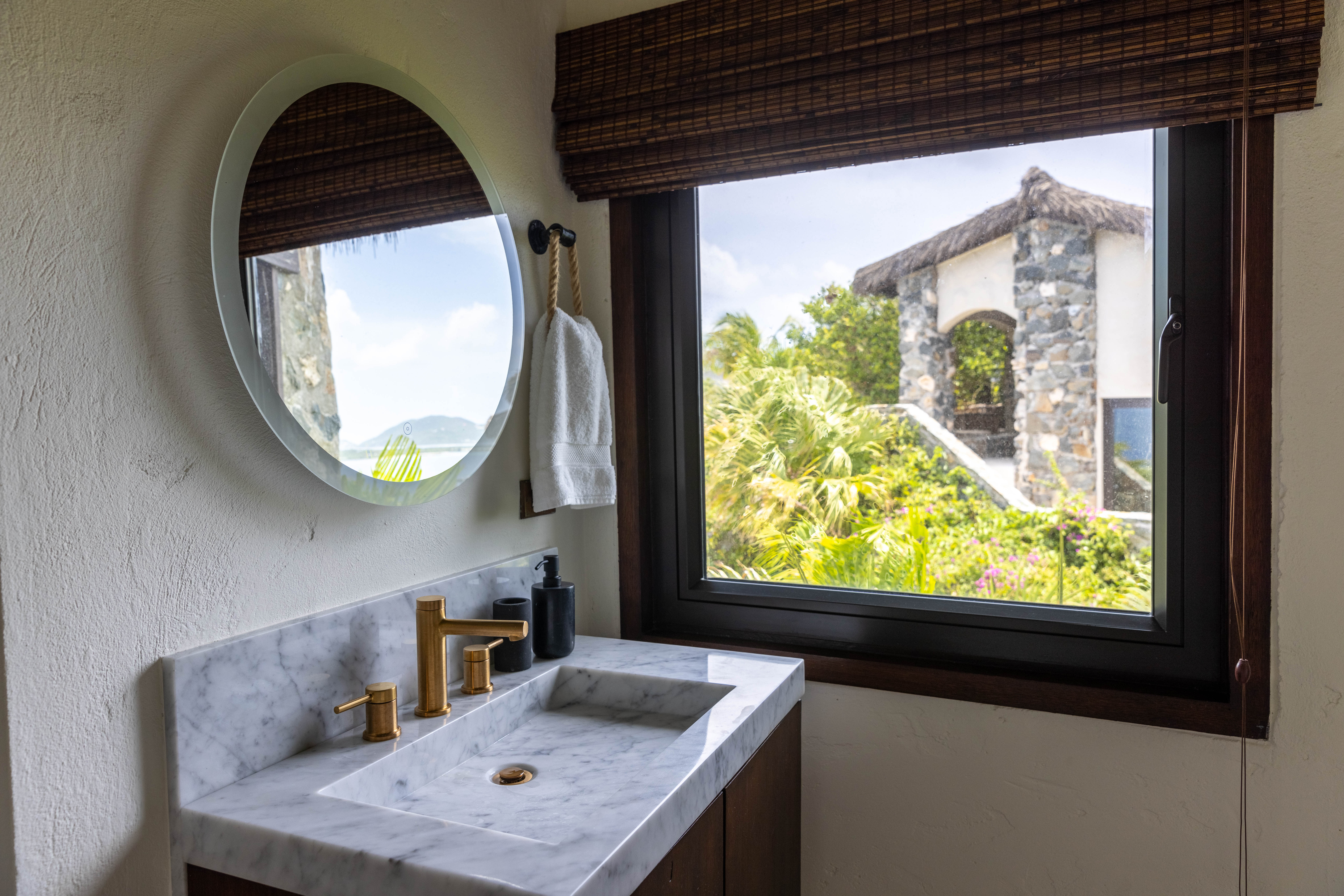 image Spacious bathroom with round mirror, natural textures, and tropical views.