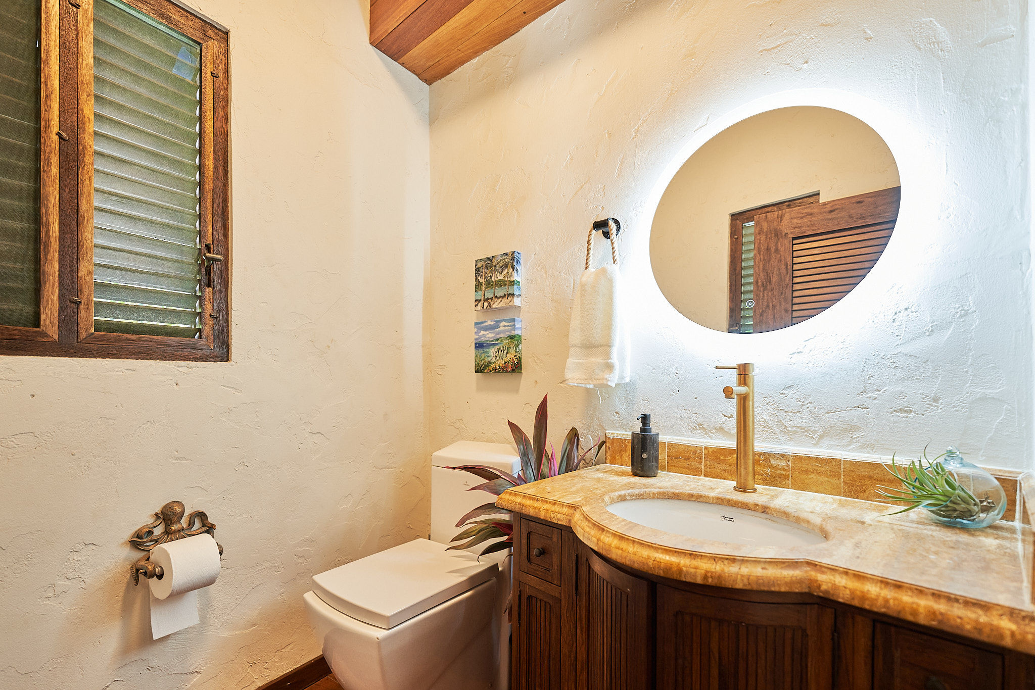 image Rustic bathroom with curved vanity, round backlit mirror, and wooden shuttered window.