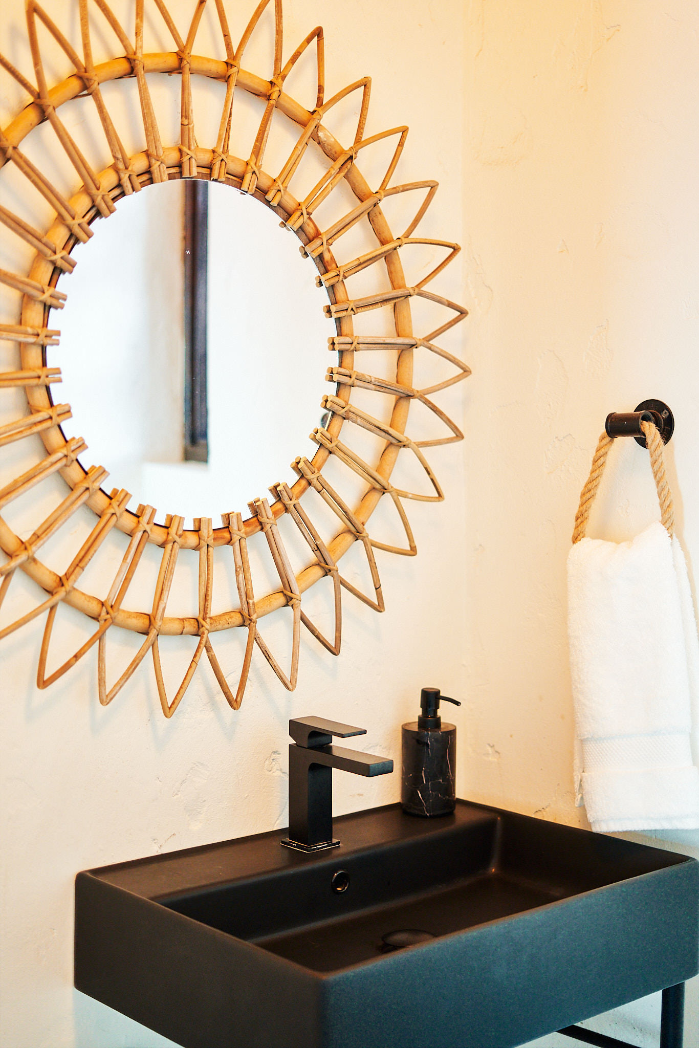 image Stylish bathroom with a woven sunburst mirror and modern black vanity.