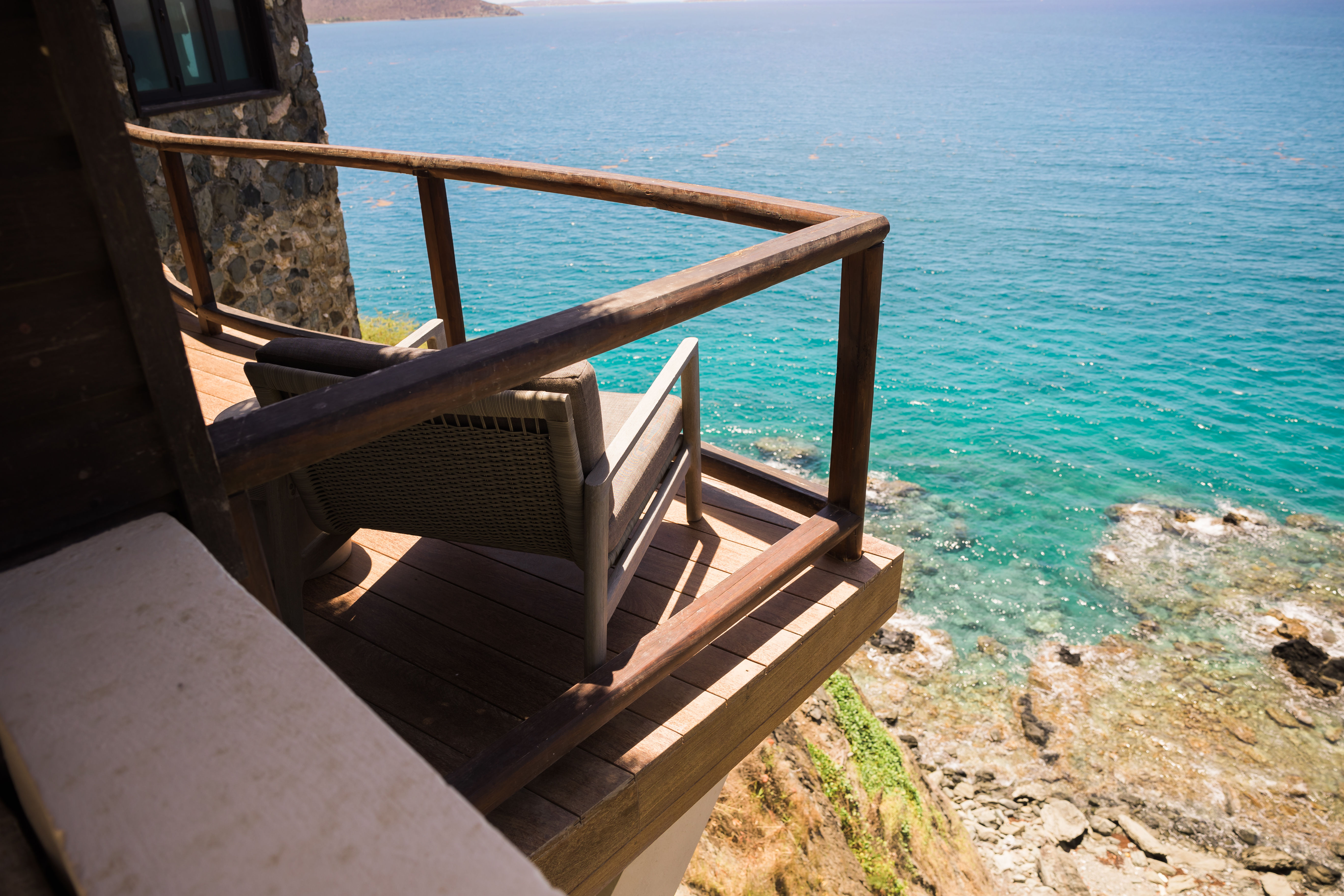 image Cozy deck seating perched above crystal-clear turquoise waters and rocky shoreline.