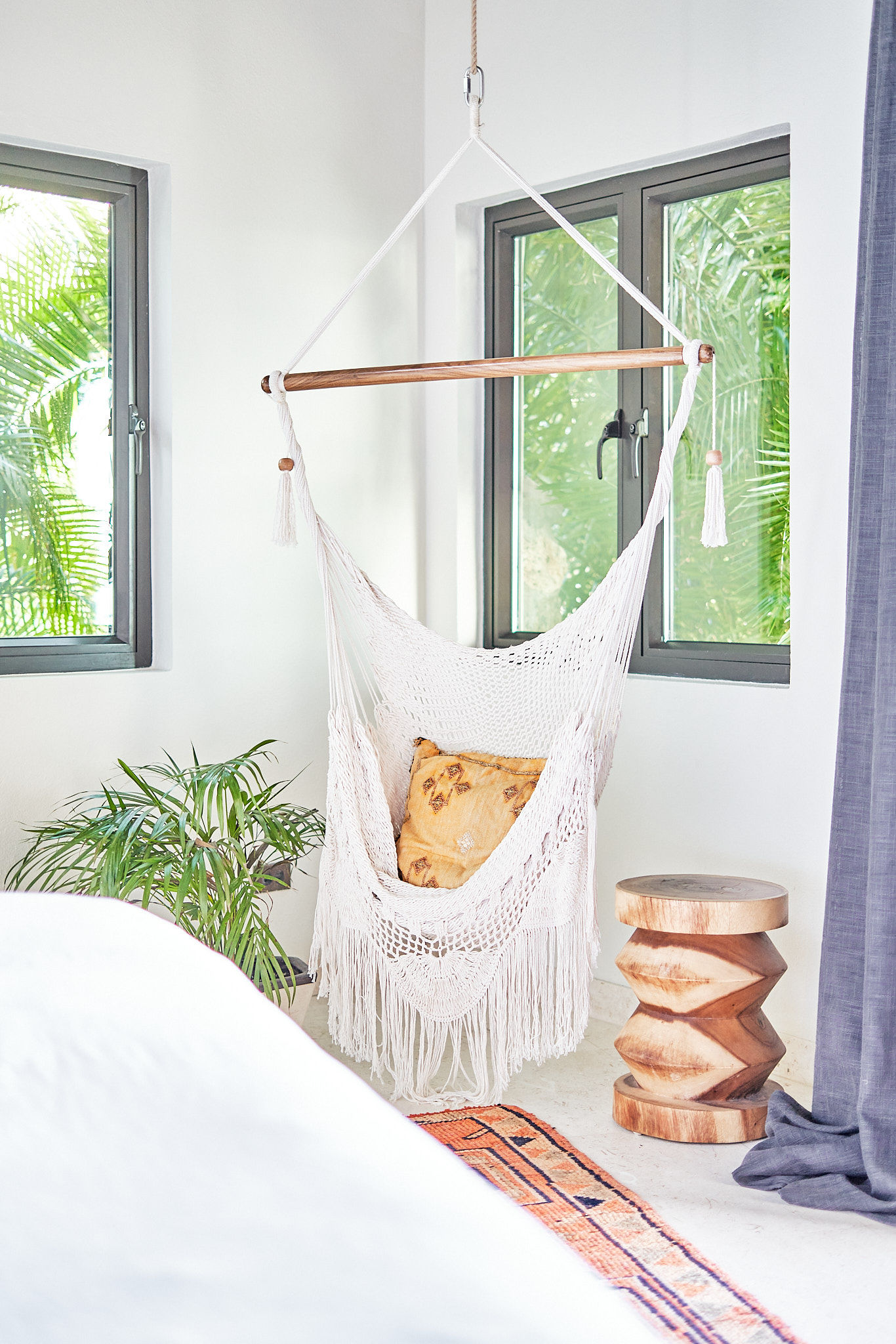 image A relaxing bedroom corner with a hanging chair and leafy views through clear windows.