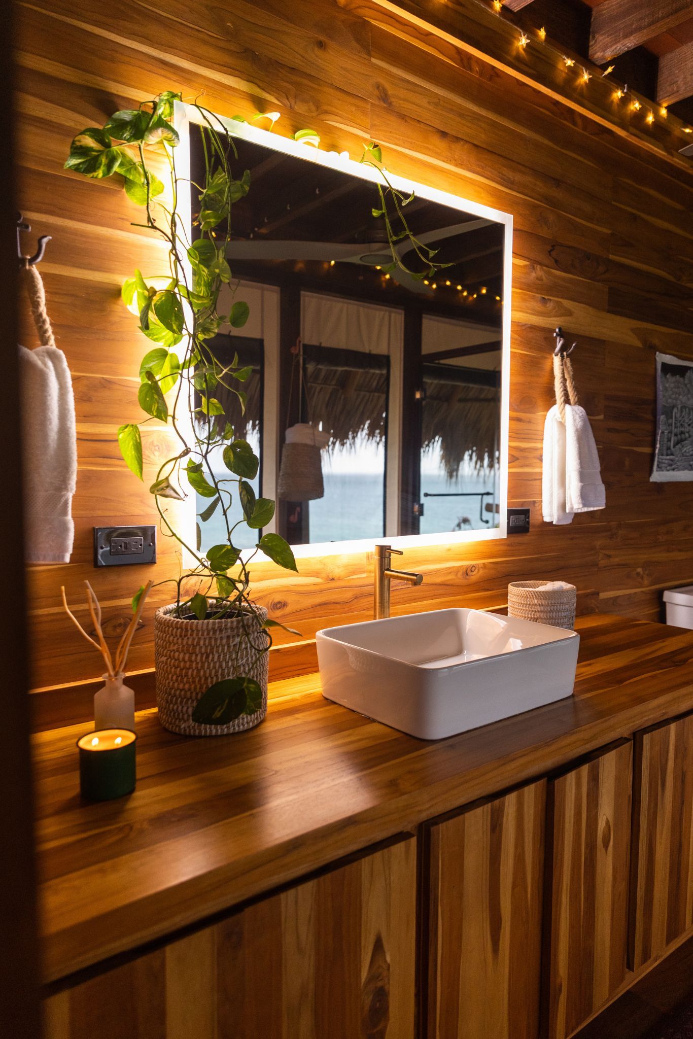 image Indulge in self-care amidst nature; the inviting wooden vanity, adorned with lush greenery, provides a serene space to refresh as the ocean whispers just beyond.